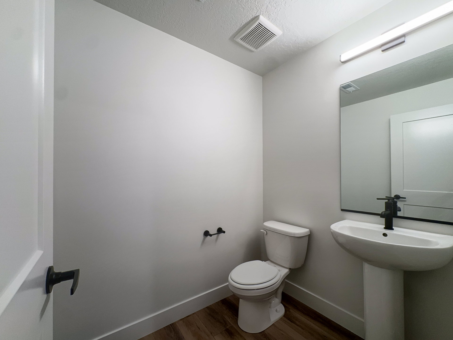 Pedestal sink with black matte faucet, accompanied by a rectangular mirror with a black frame