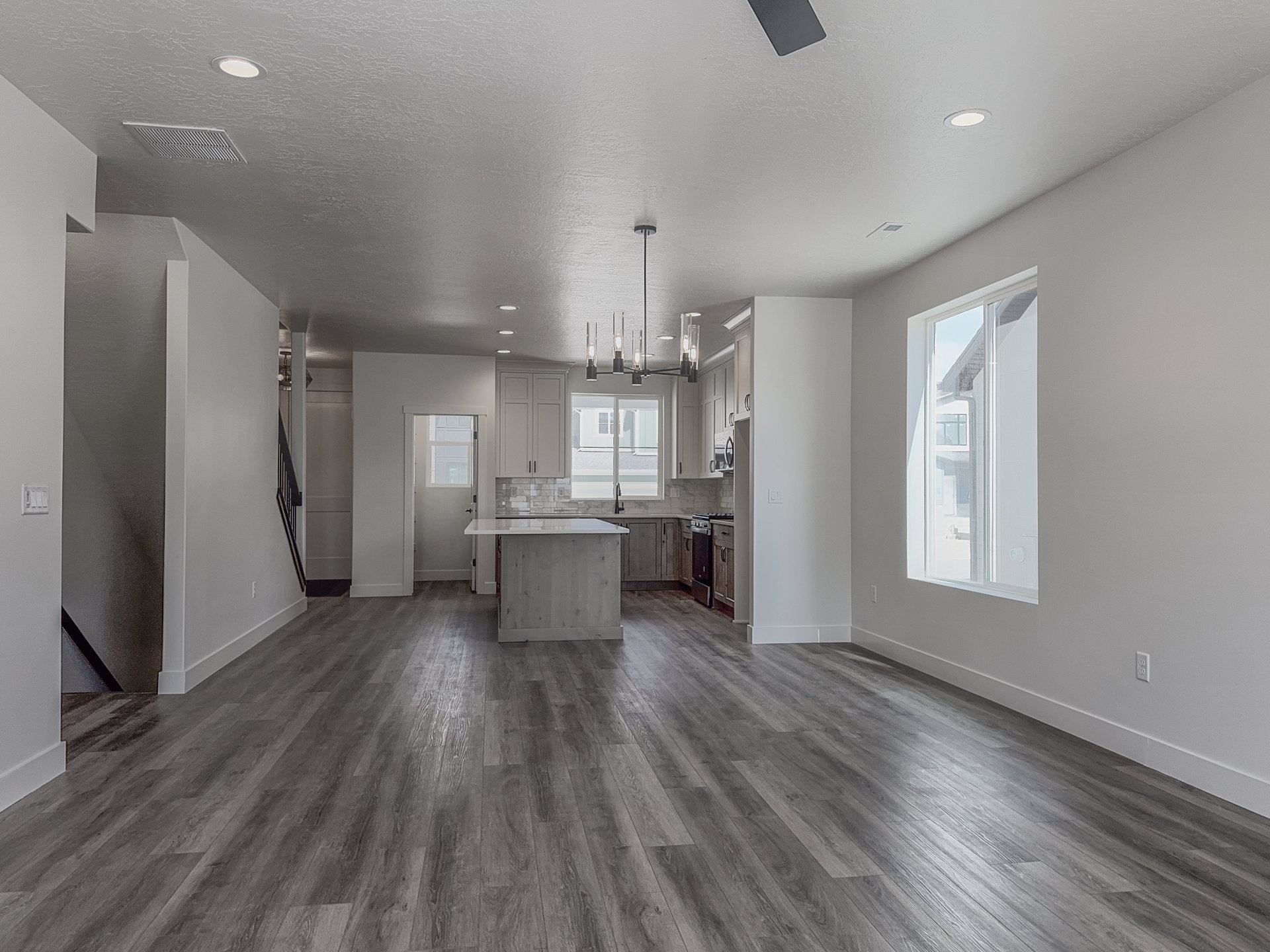 Open-concept living area featuring wood-finish flooring, a kitchen island with stone countertop, stainless steel appliances, and recessed lighting