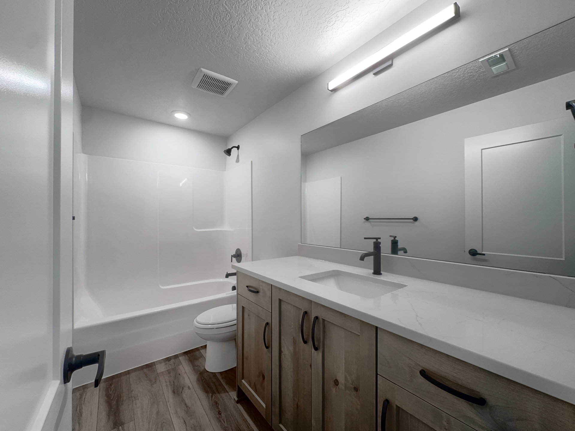 Bathroom featuring a spacious vanity with wood-finish cabinetry, a large integrated mirror, and a white countertop with an undermount sink