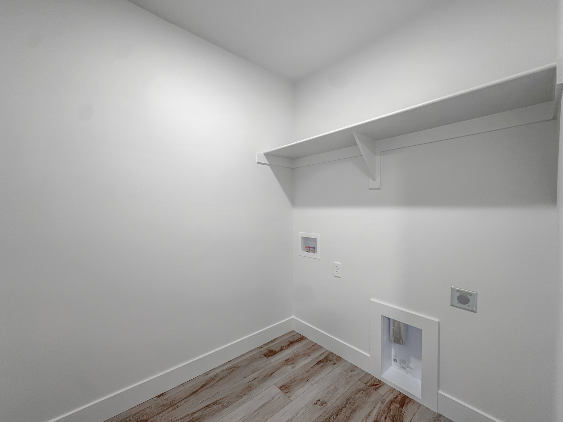 Dedicated laundry space featuring wood-finish flooring, white walls, and a built-in wall shelf