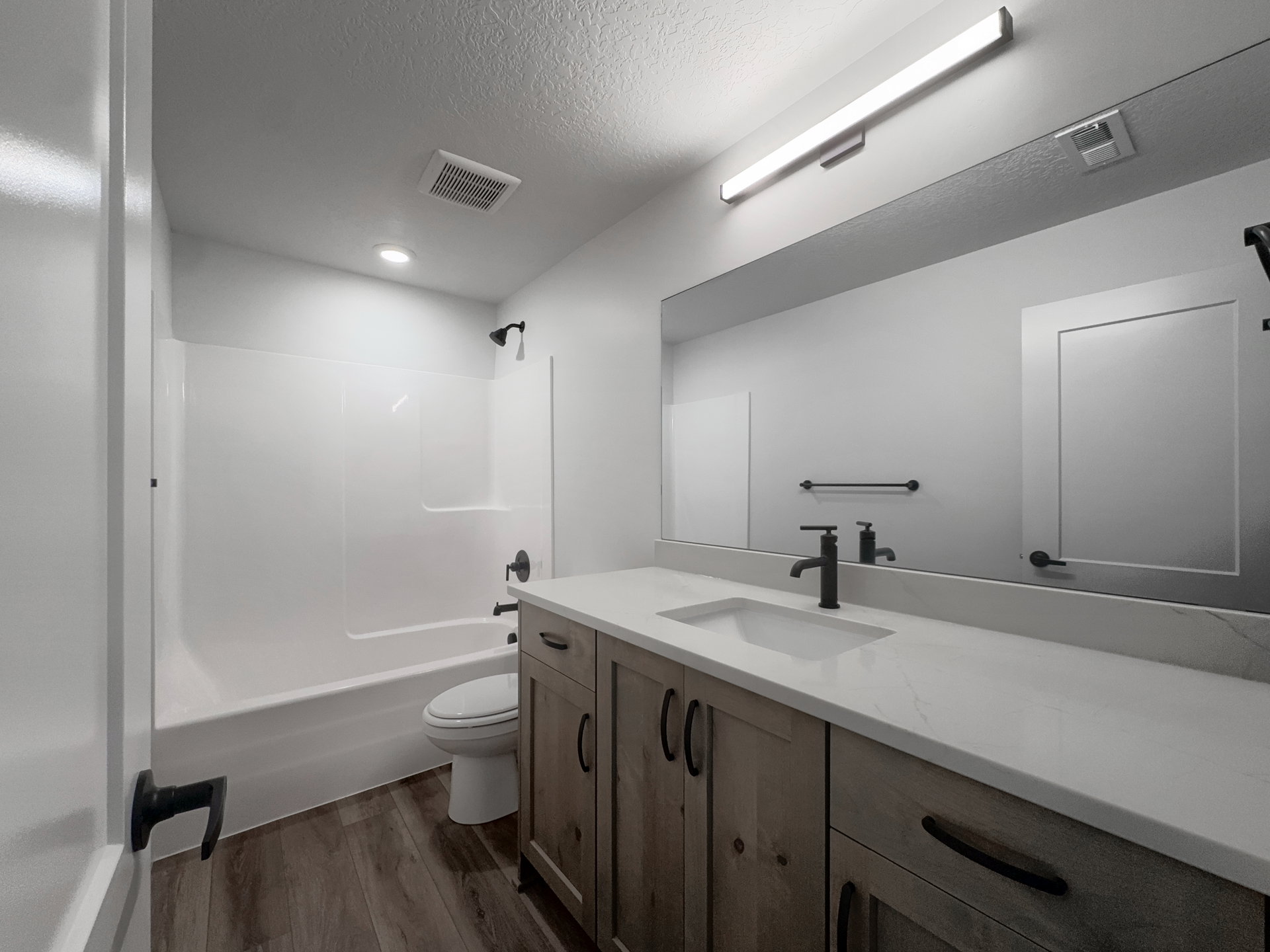 Bathroom featuring a wood-finish vanity with a light-toned countertop, integrated sink, and matte black fixtures