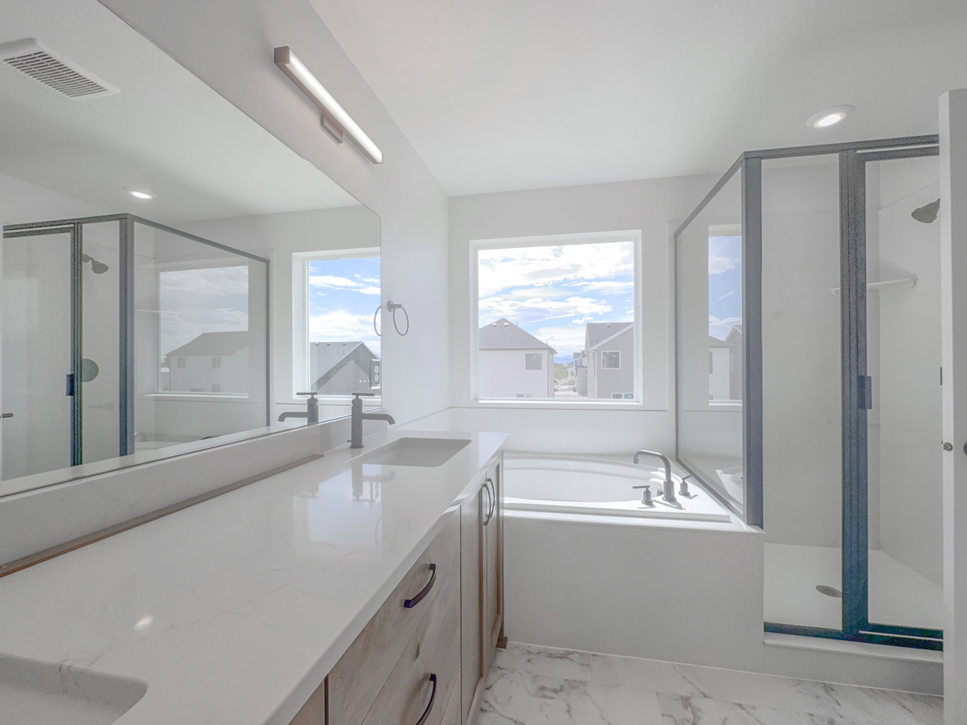 Contemporary bathroom featuring a built-in tub, separate shower with glass enclosure, dual vanity with undermount sinks, and light wood-finish cabinetry