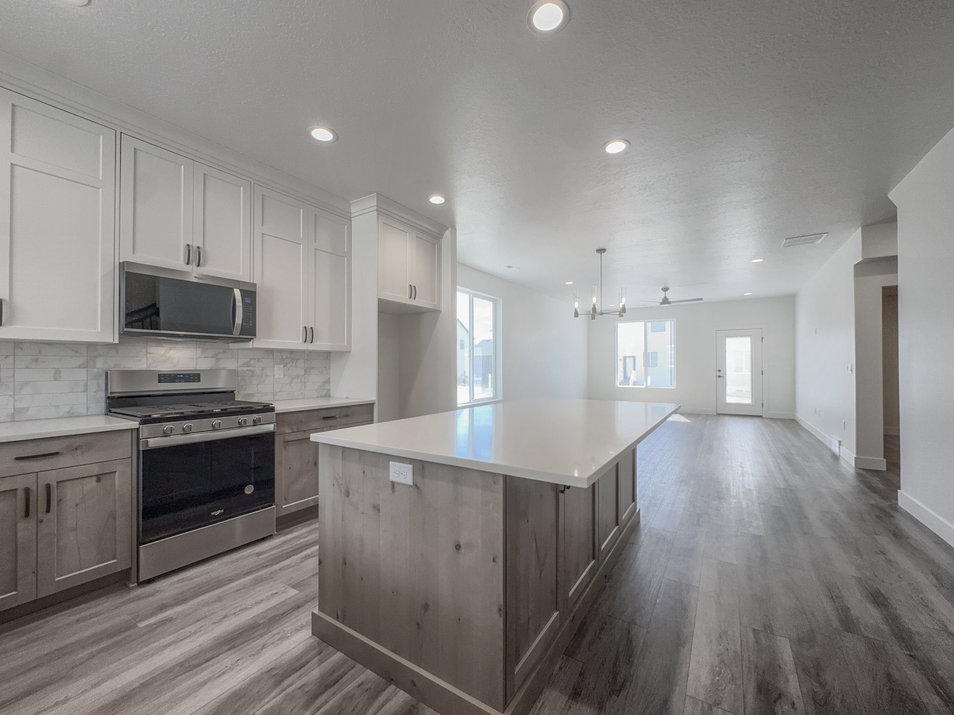 Open-concept kitchen and living area featuring a large center island with a light-toned countertop, two-tone cabinetry, stainless steel range and microwave, and wood-finish flooring