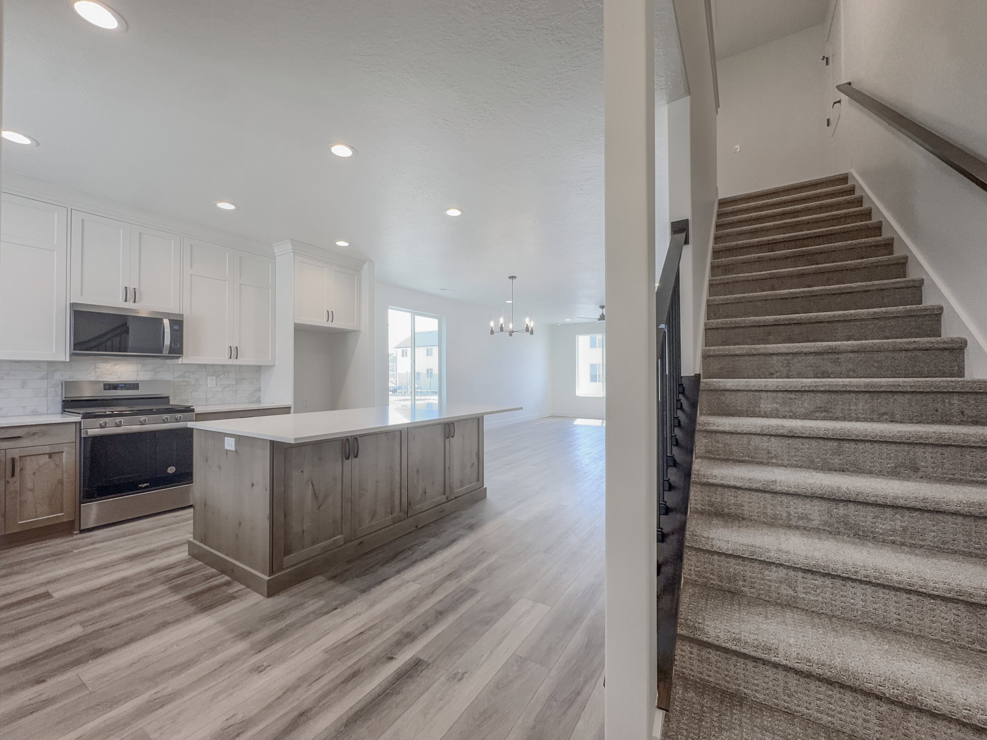 Contemporary kitchen featuring white upper cabinetry, a coordinating wood-finish island with a light countertop, stainless steel appliances, and wood-finish flooring