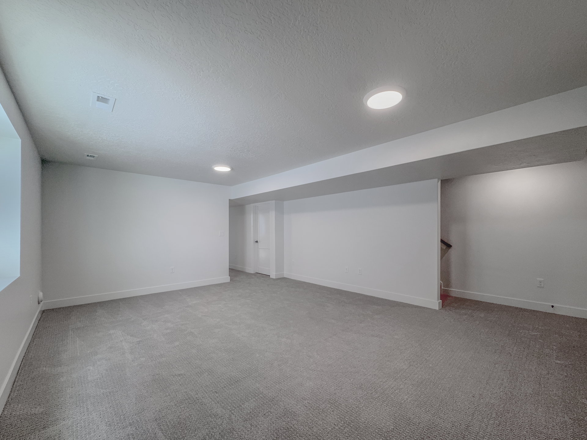 Spacious room featuring neutral carpeting, white walls, recessed lighting, and a visible doorway