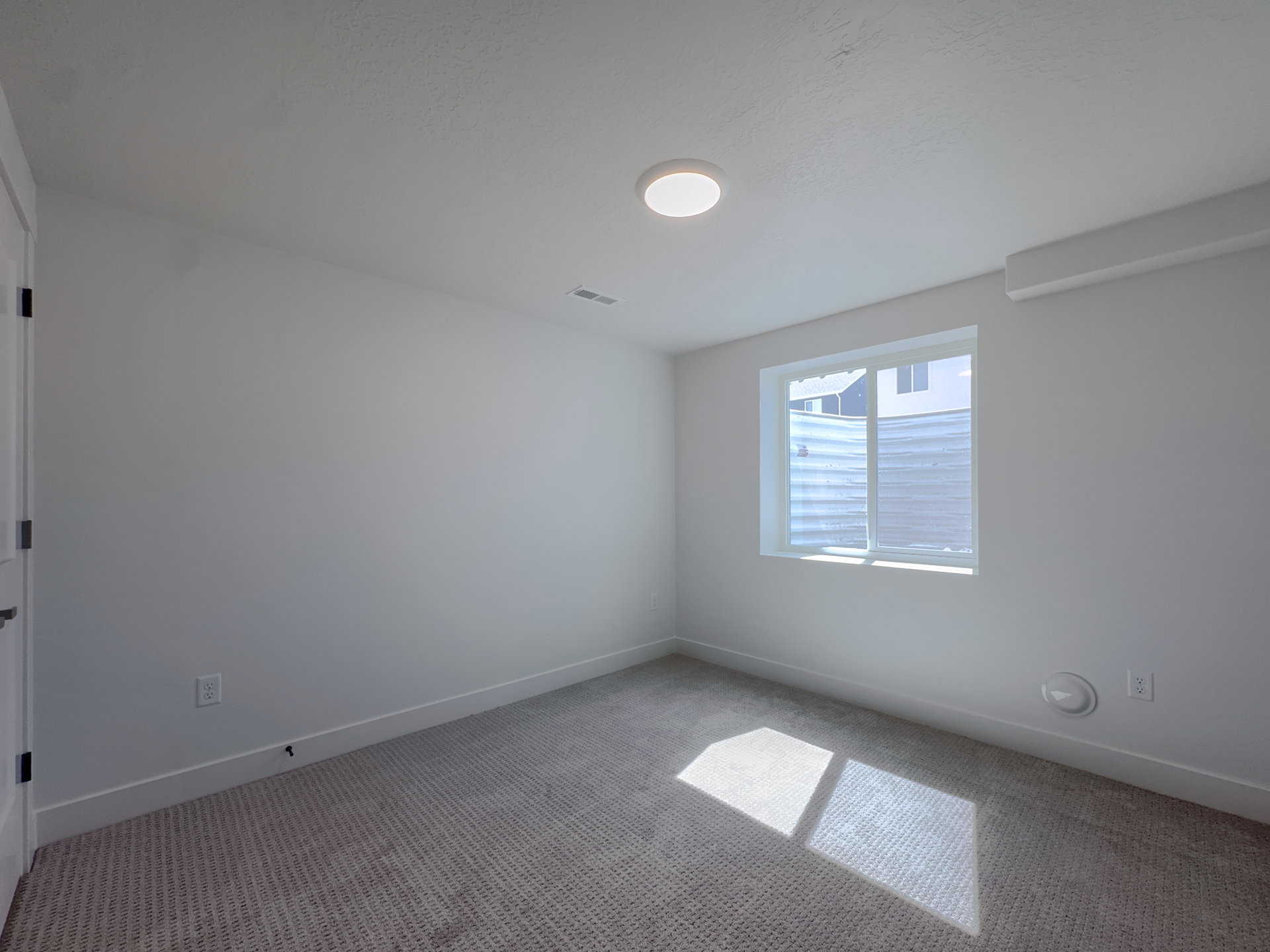 Bright room featuring a window, neutral carpet, white baseboards, and a flush-mount ceiling light