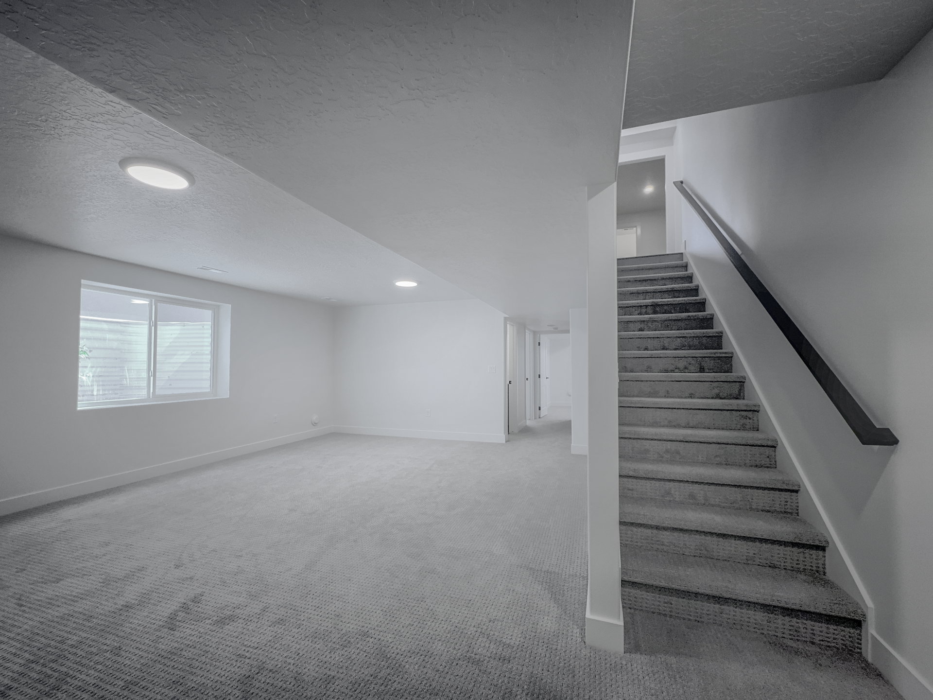 Carpeted staircase with a dark handrail leading to a lower level featuring recessed lighting, a window, and light gray wall-to-wall carpeting