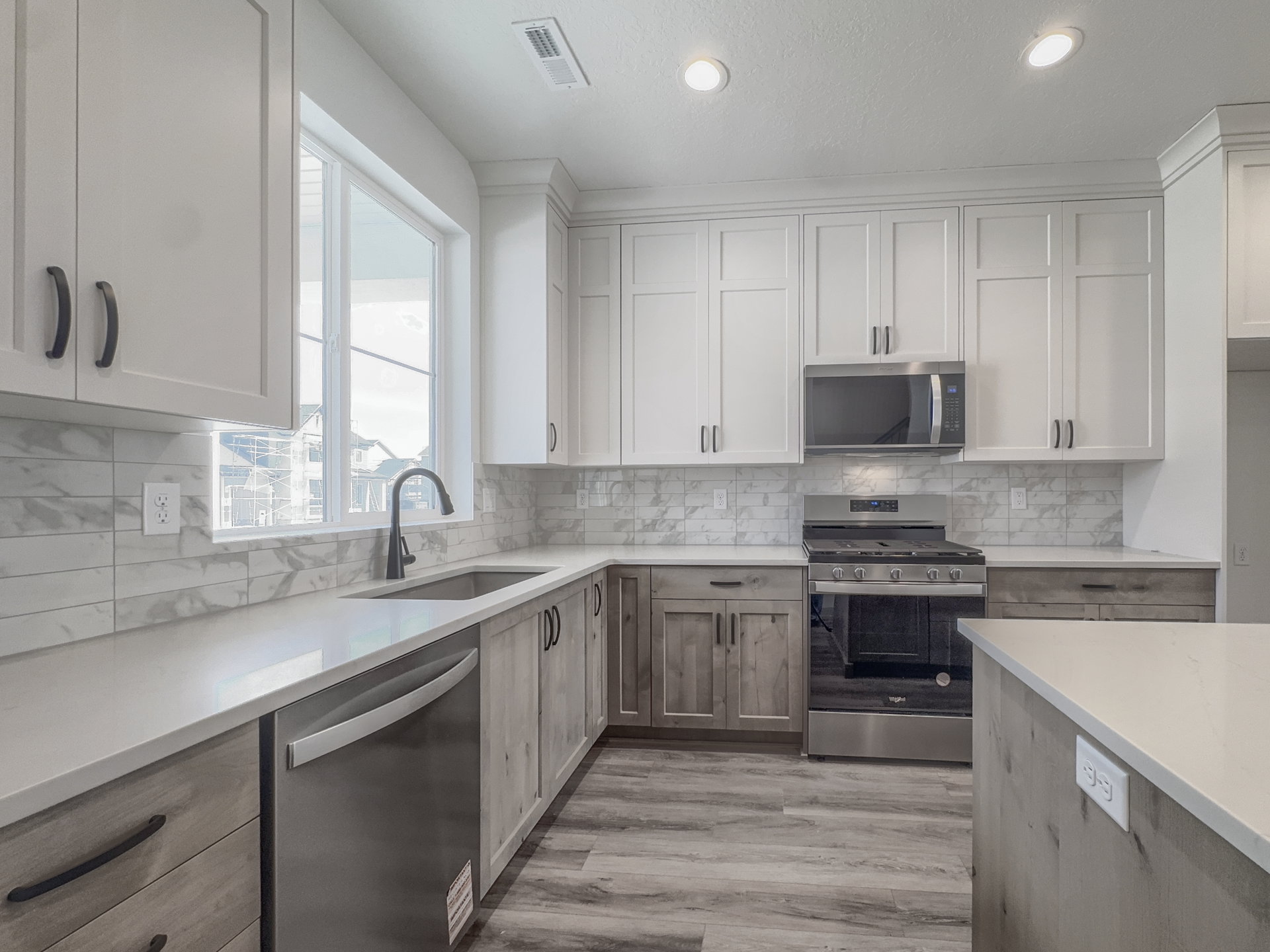 Modern kitchen featuring two-tone cabinetry, stainless steel appliances, a white solid surface countertop, and a tiled backsplash