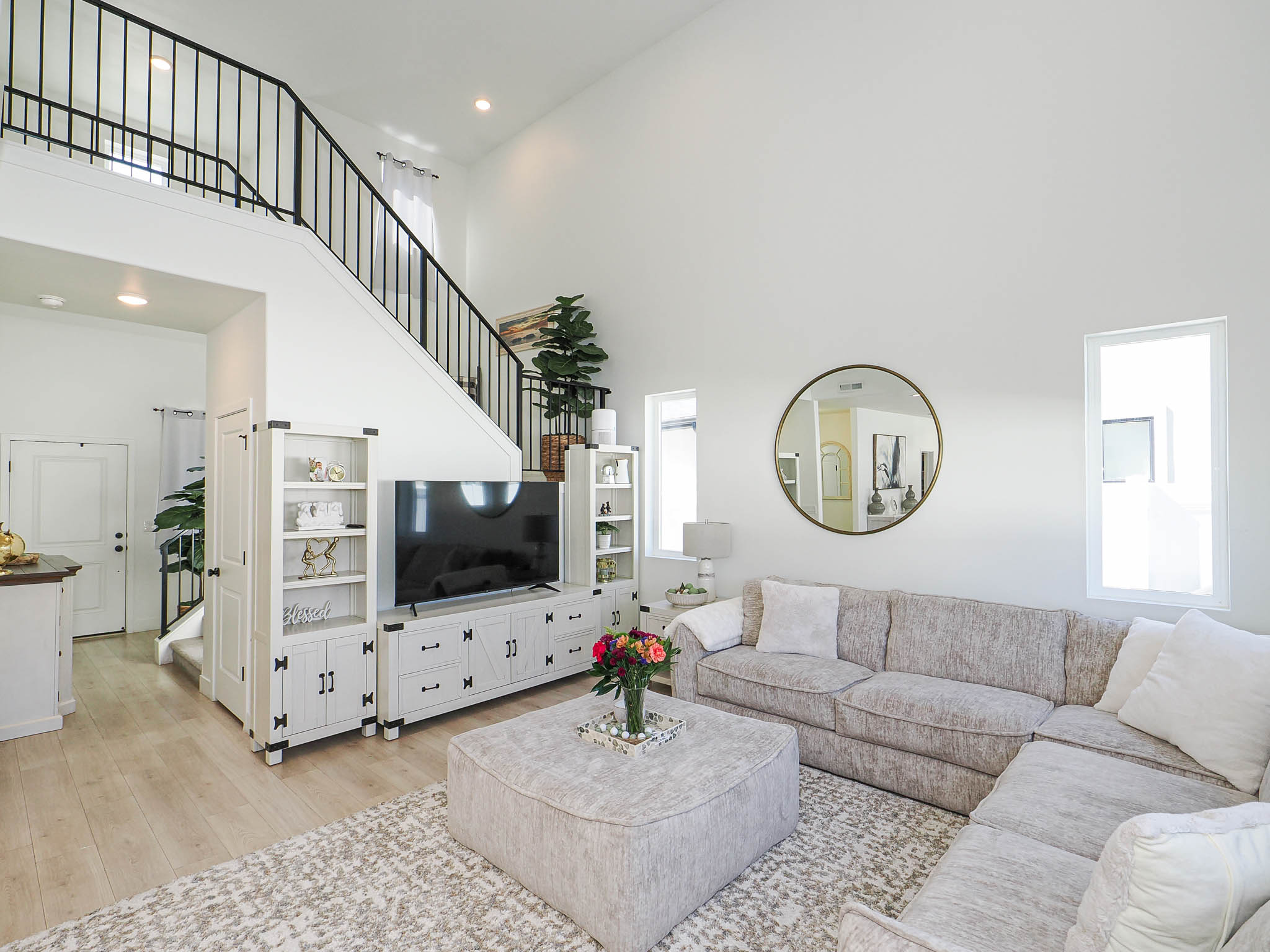 Great room featuring light wood-finish flooring, high vaulted ceilings, and a black metal spindle staircase
