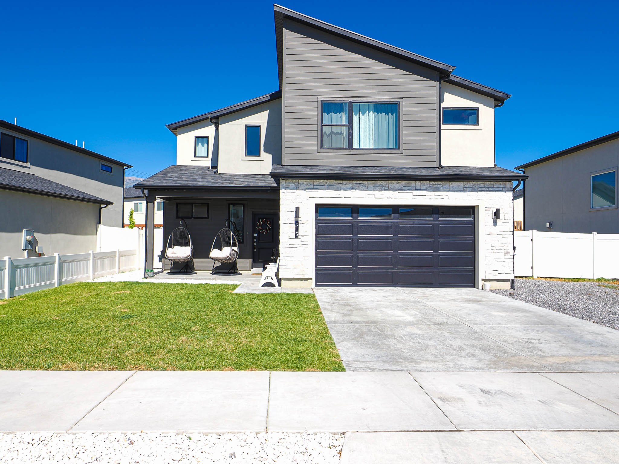 Contemporary facade featuring a prominent two-car garage, partial stone veneer, and a covered front porch