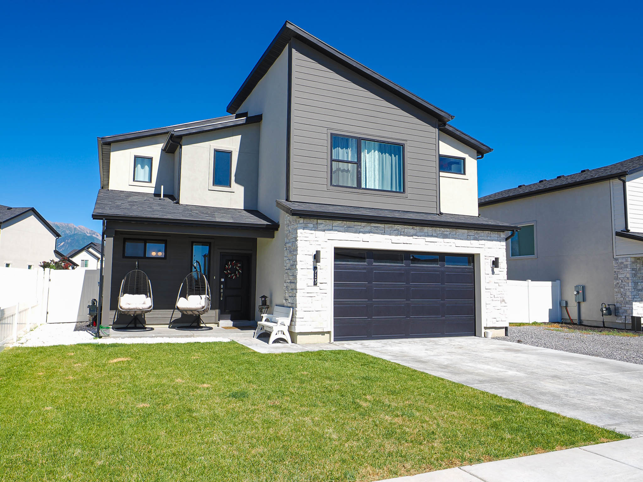 Modern facade featuring a combination of light stucco, dark gray siding, and stacked stone accents