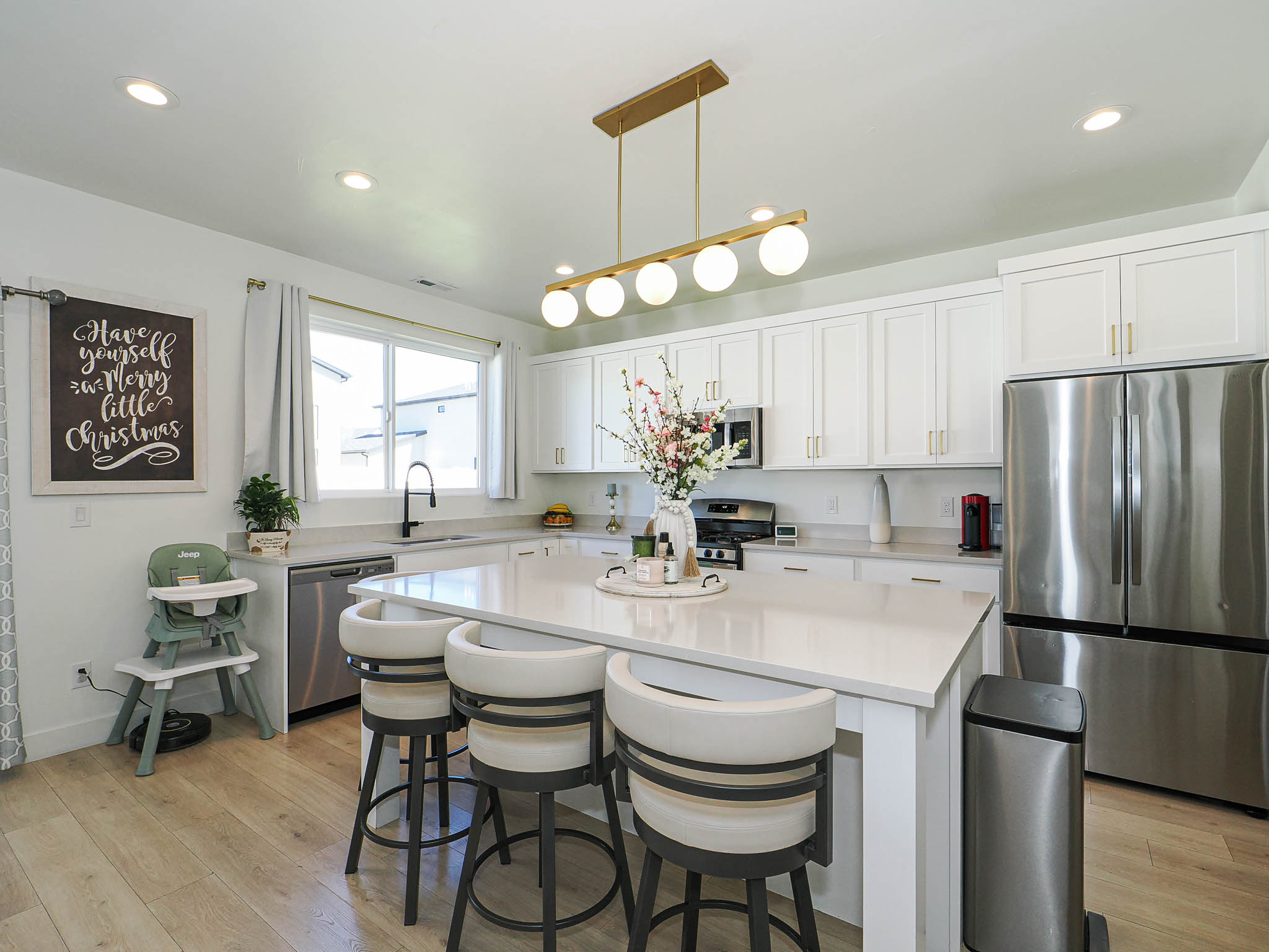 Modern kitchen featuring a large central island with seating, stainless steel appliances, abundant white cabinetry with gold-tone hardware, wood-finish flooring, and recessed ceiling lights