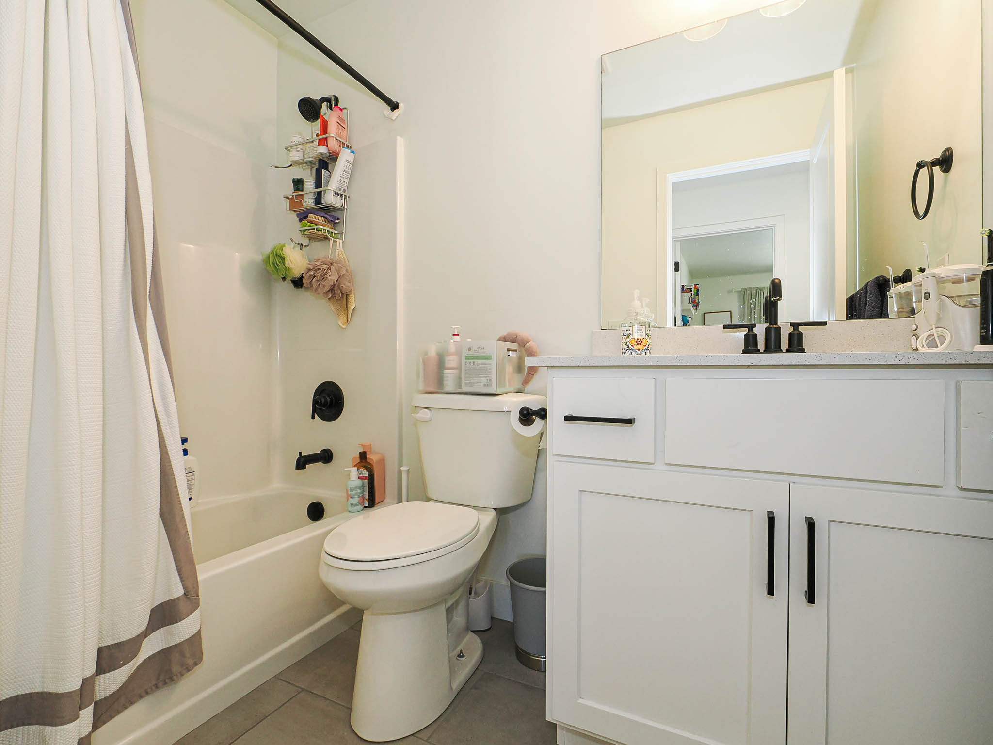 White shaker-style vanity with matte black hardware, a light-toned countertop, and an undermount sink