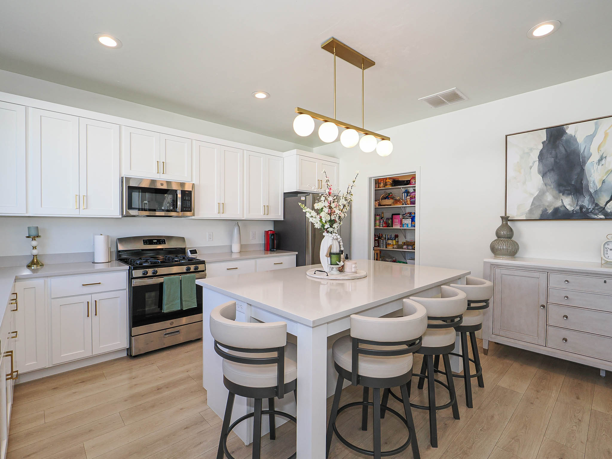 Modern kitchen featuring a central island with seating for four, white shaker-style cabinetry, stainless steel appliances, wood-finish flooring, and a walk-in pantry