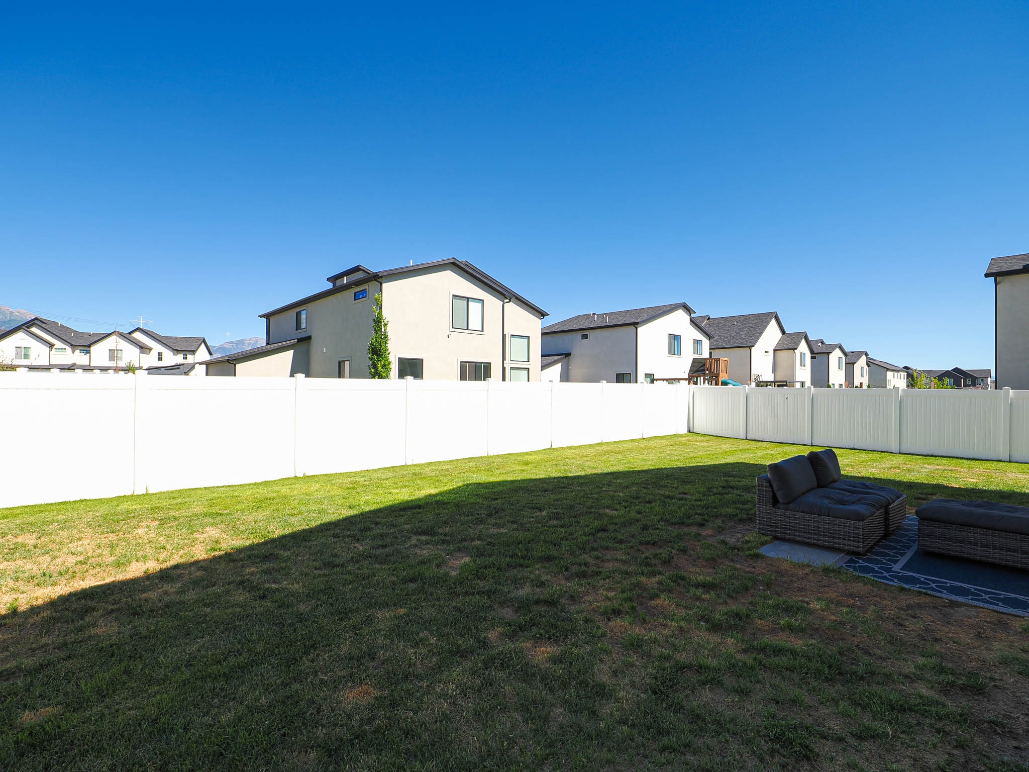 Spacious, enclosed backyard featuring a white vinyl fence and a green lawn