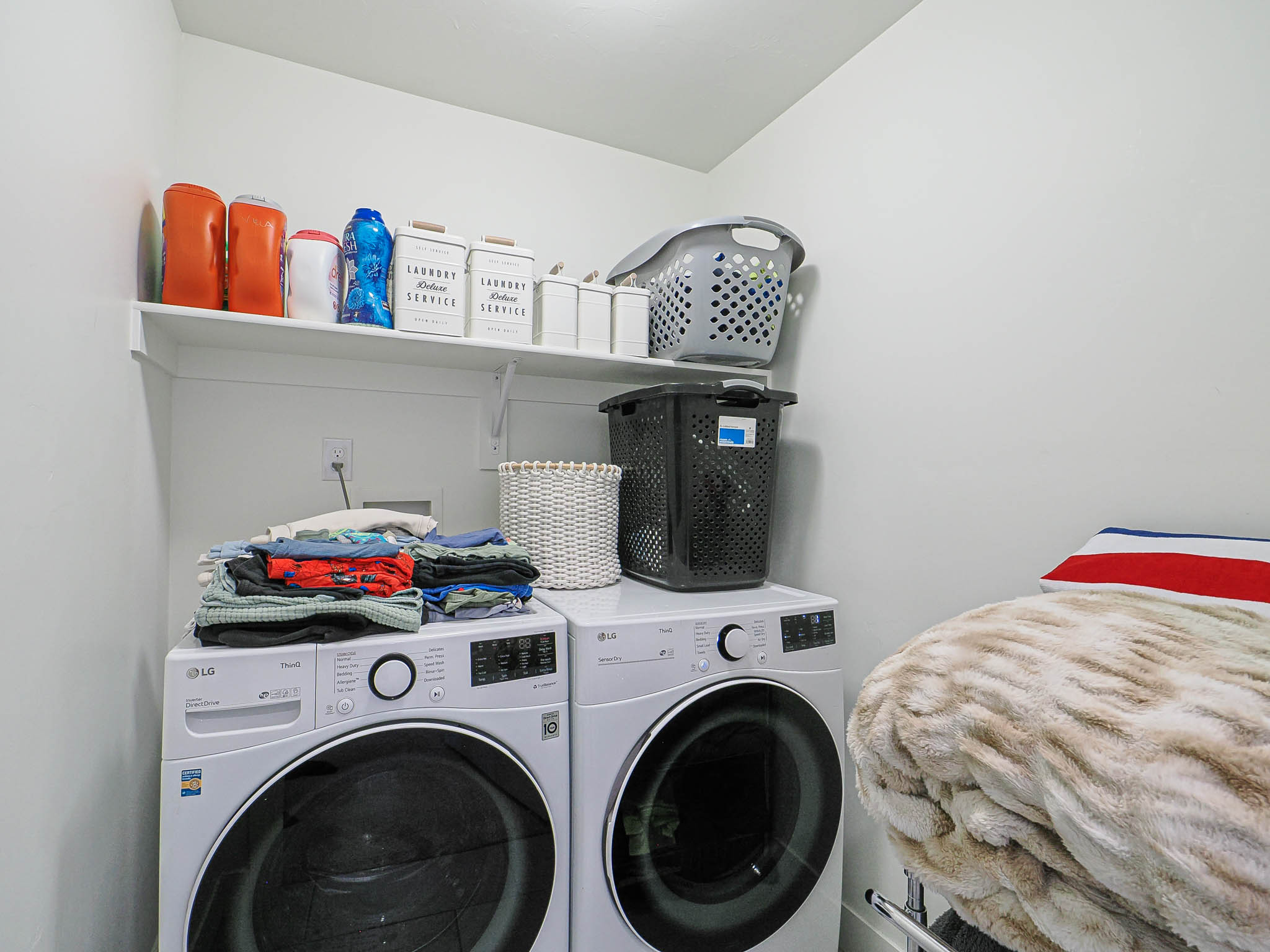 Dedicated laundry area featuring a white wall shelf, built-in wall outlet, and light-colored walls