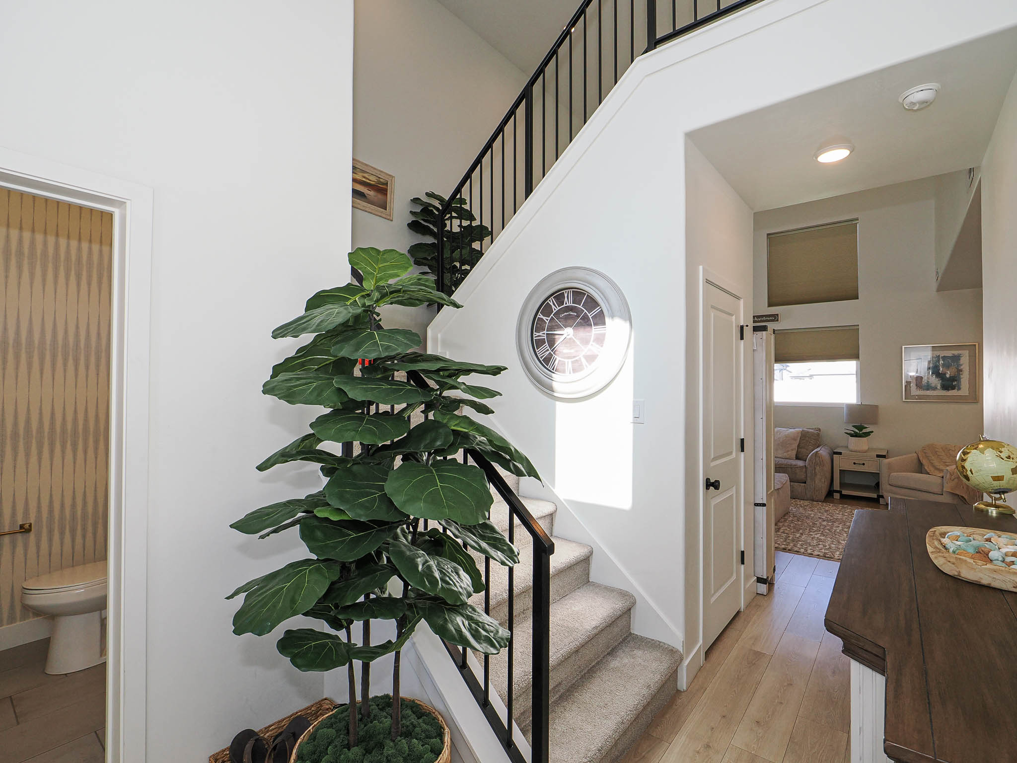 Two-story foyer with wood-finish flooring, a carpeted staircase with black iron railings, and a powder room featuring patterned wallpaper and a white toilet
