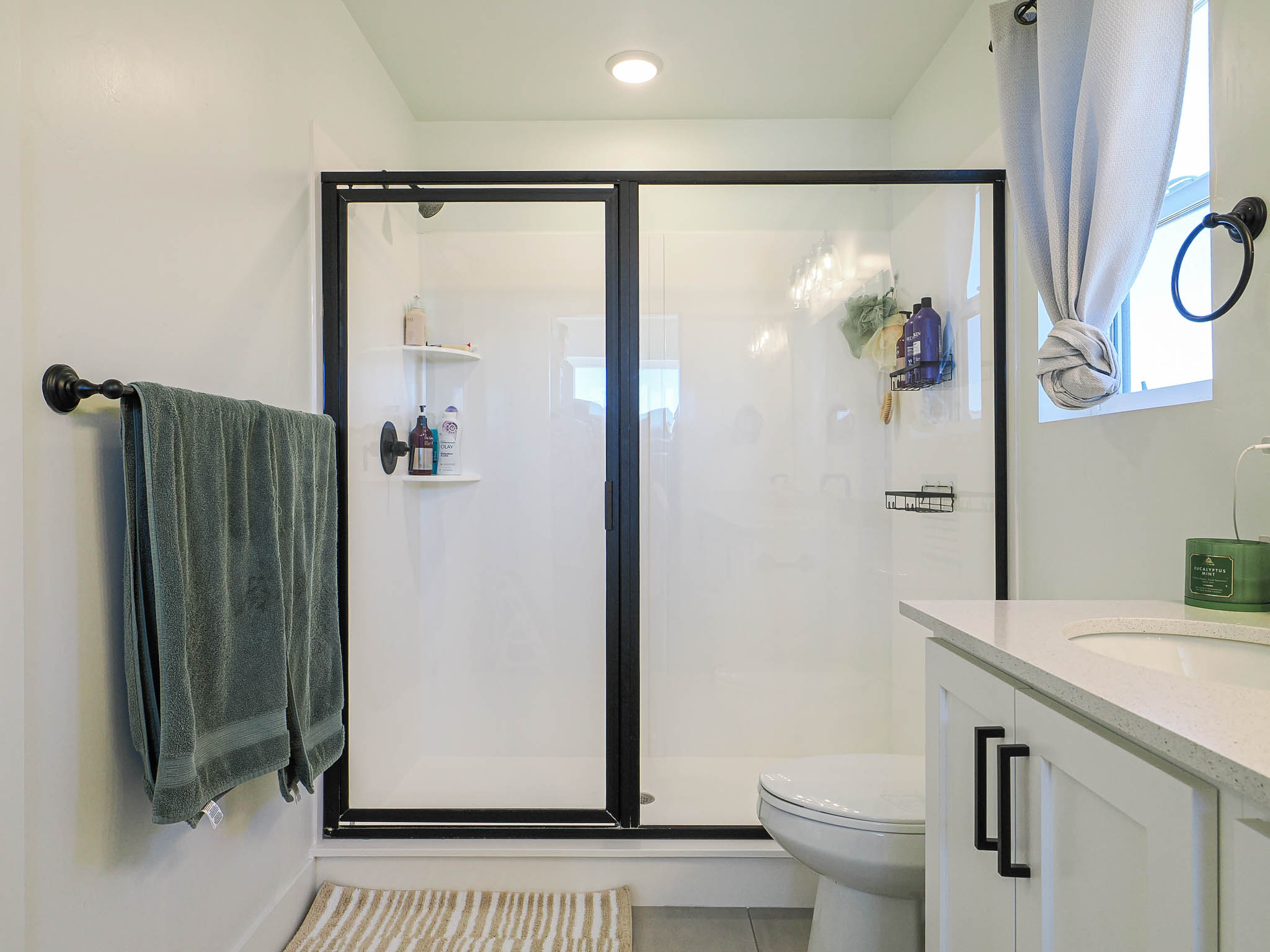 Bathroom featuring a modern shower enclosure with black framing, integrated shower shelving, a white vanity with a quartz-finish countertop, and a contemporary toilet