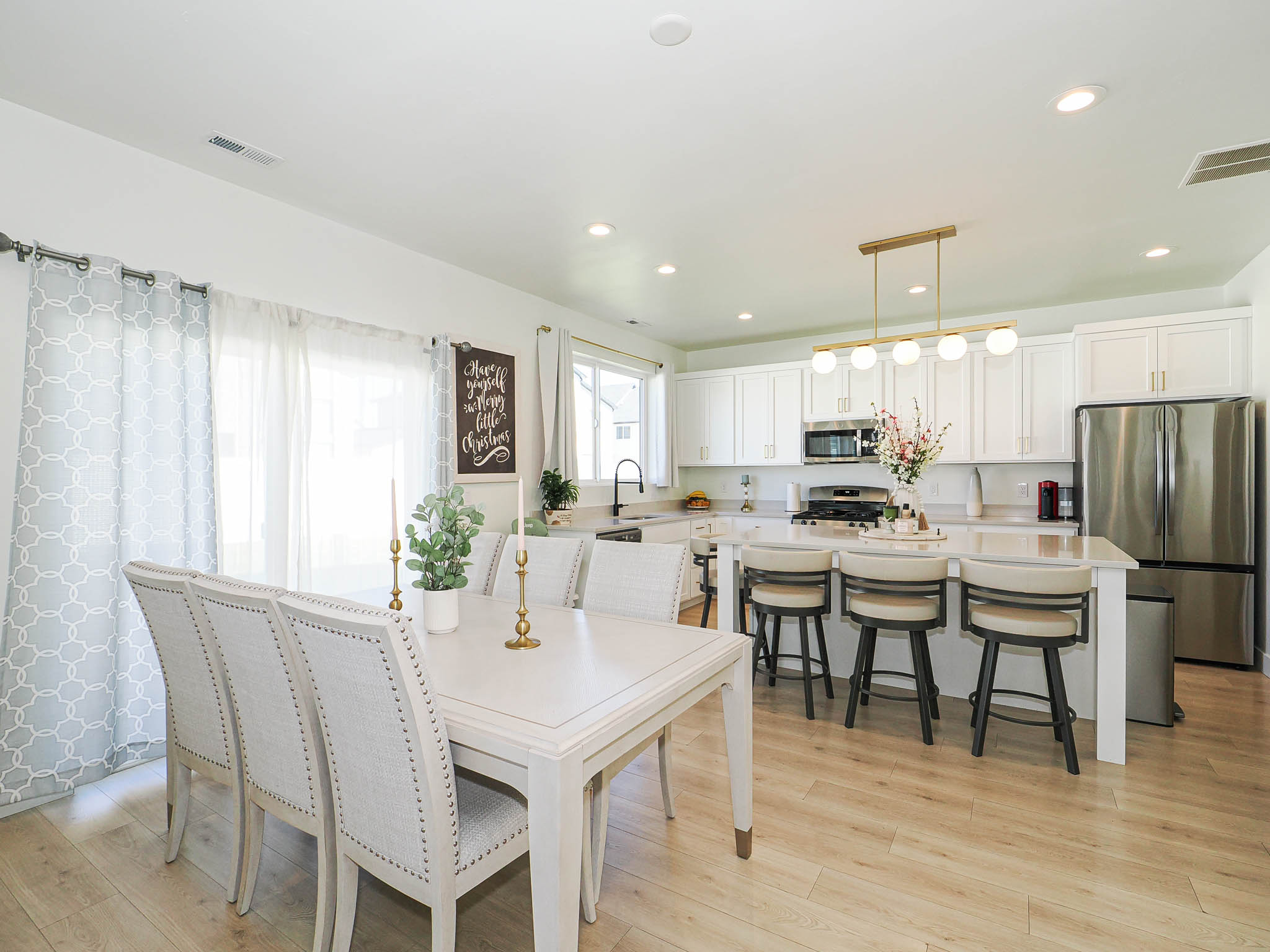 Open-concept kitchen and dining area featuring light wood-finish flooring, white cabinetry, a central island with bar seating, stainless steel appliances, and recessed lighting
