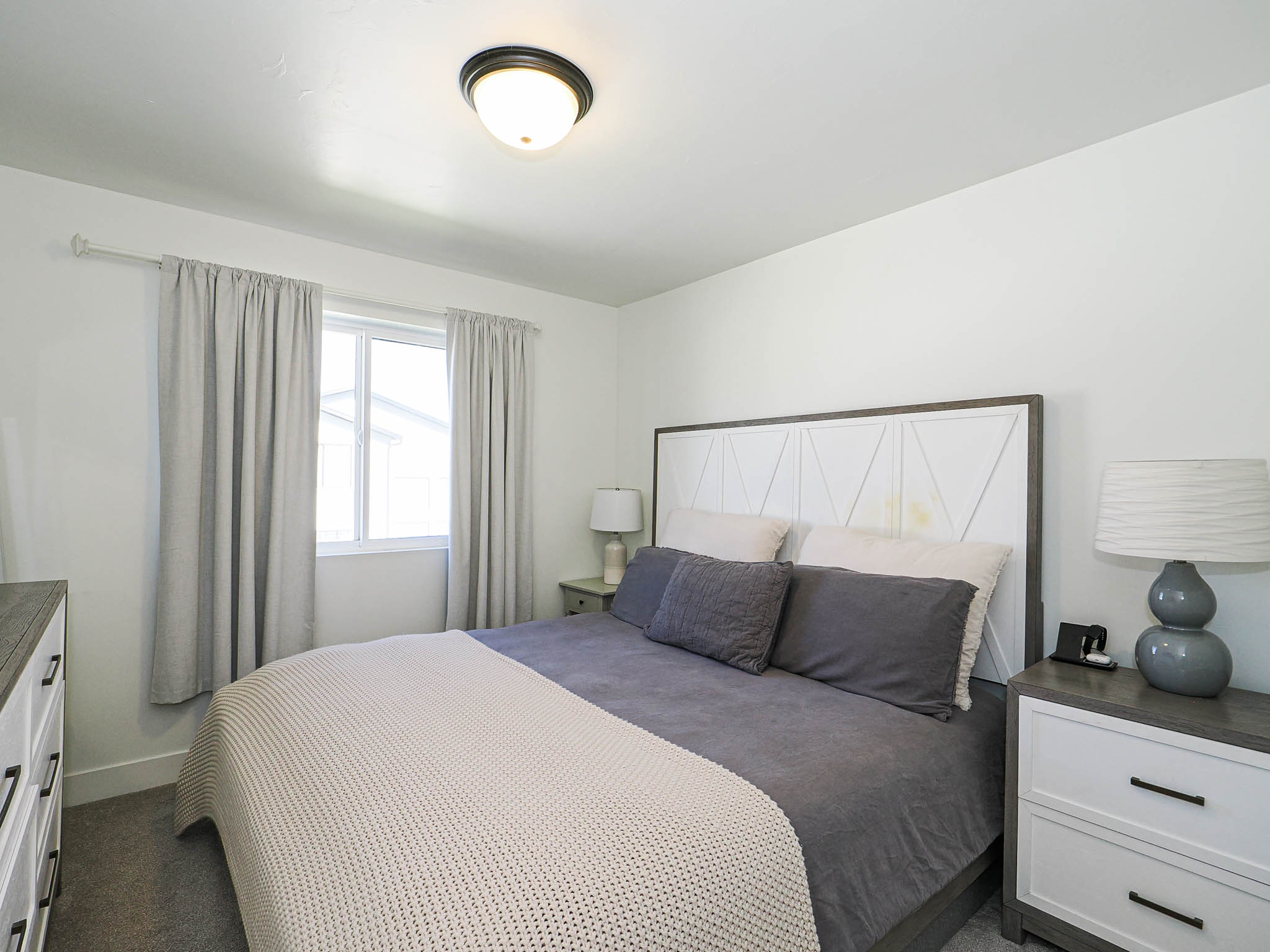 Carpeted bedroom featuring a window with natural light, a ceiling-mounted light fixture, and a decorative headboard