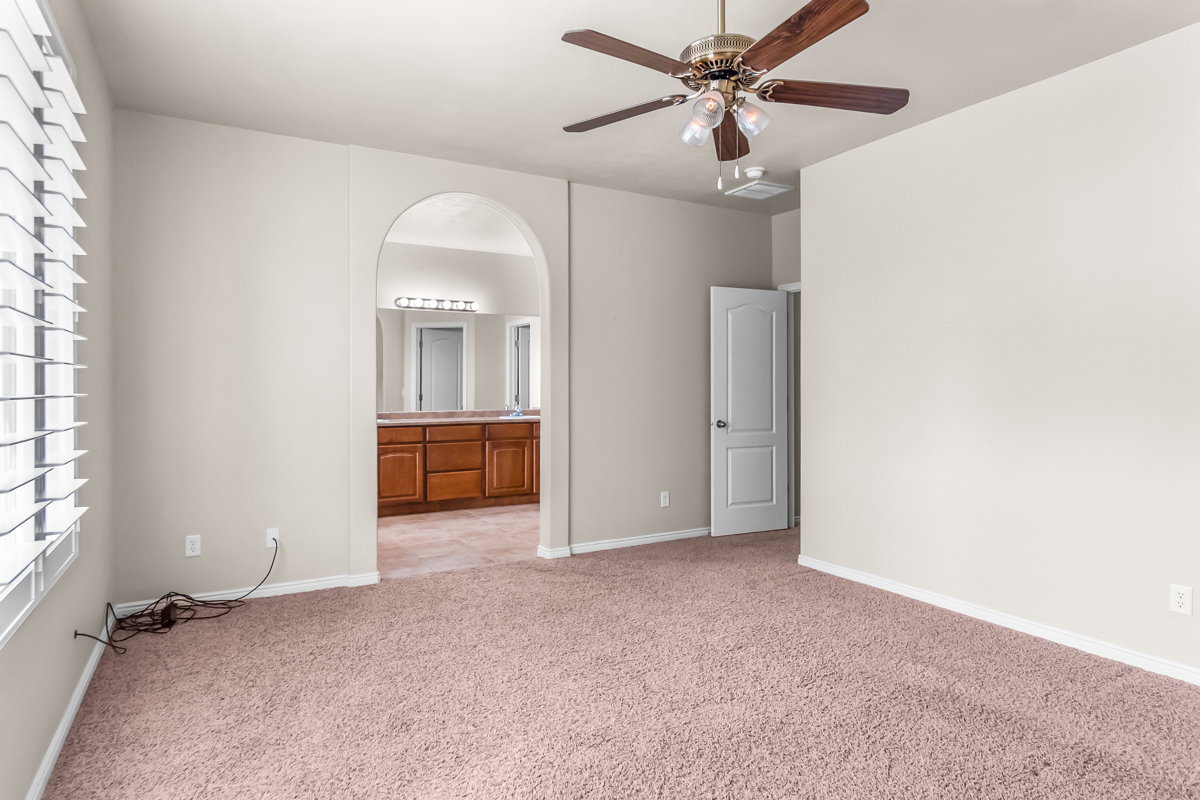 Spacious room featuring neutral paint, plush carpeting, a ceiling fan with light fixture, and arched entryway