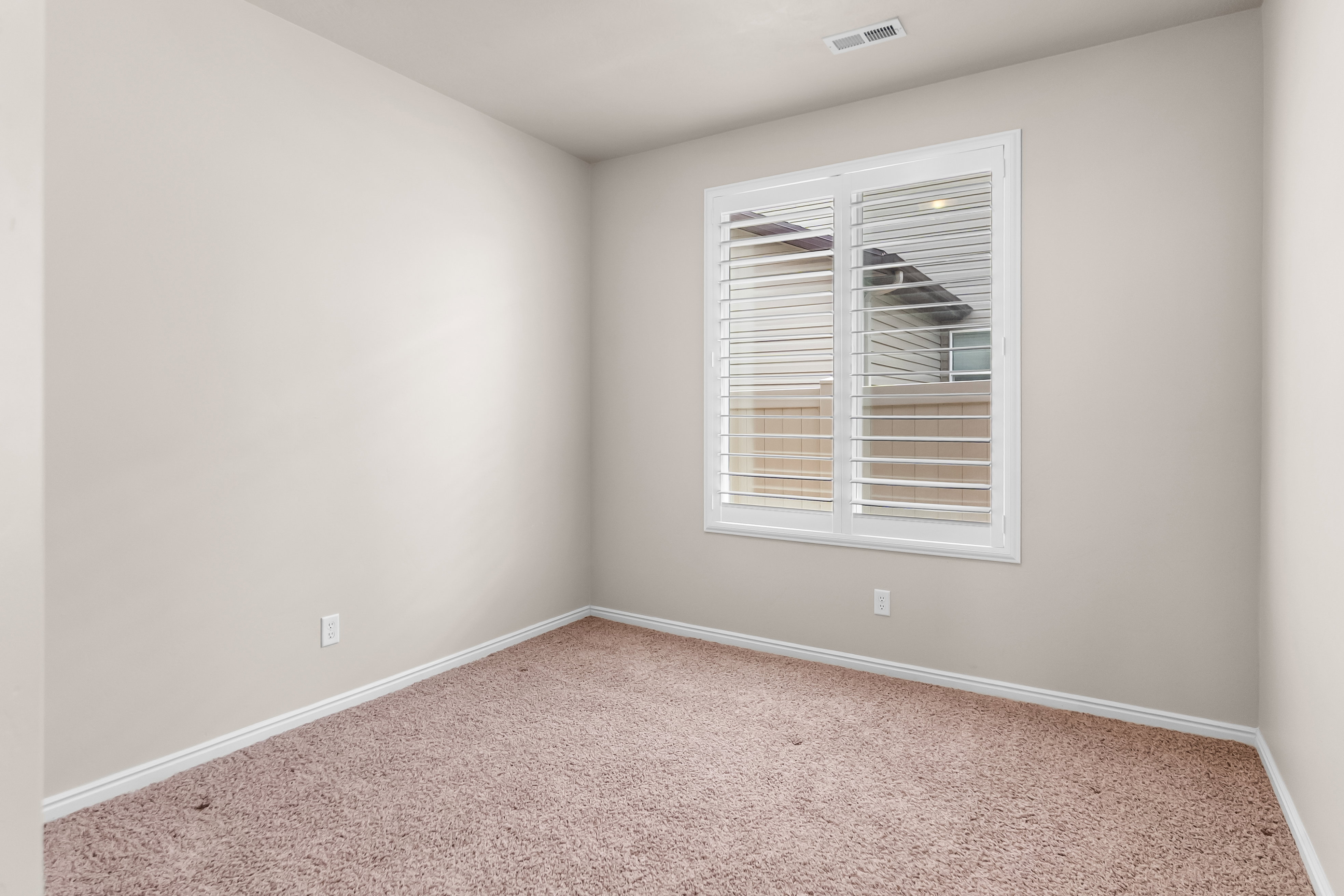 Room featuring neutral wall paint, white baseboards, plush carpet flooring, a window with white plantation shutters, and a ceiling vent