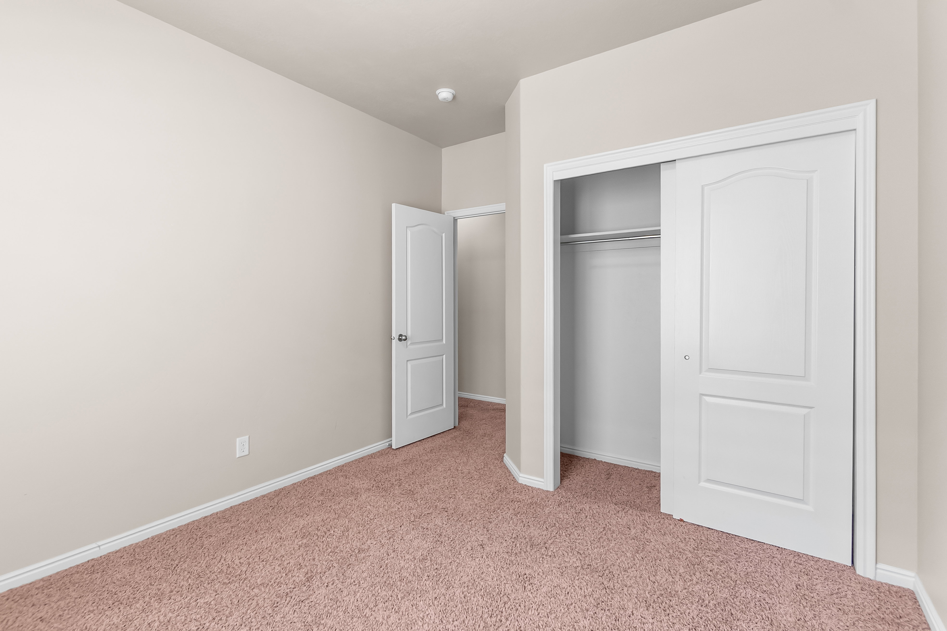 Room featuring neutral wall paint, light brown carpeting, a white interior door, and a closet with white sliding doors and an interior rod and shelf