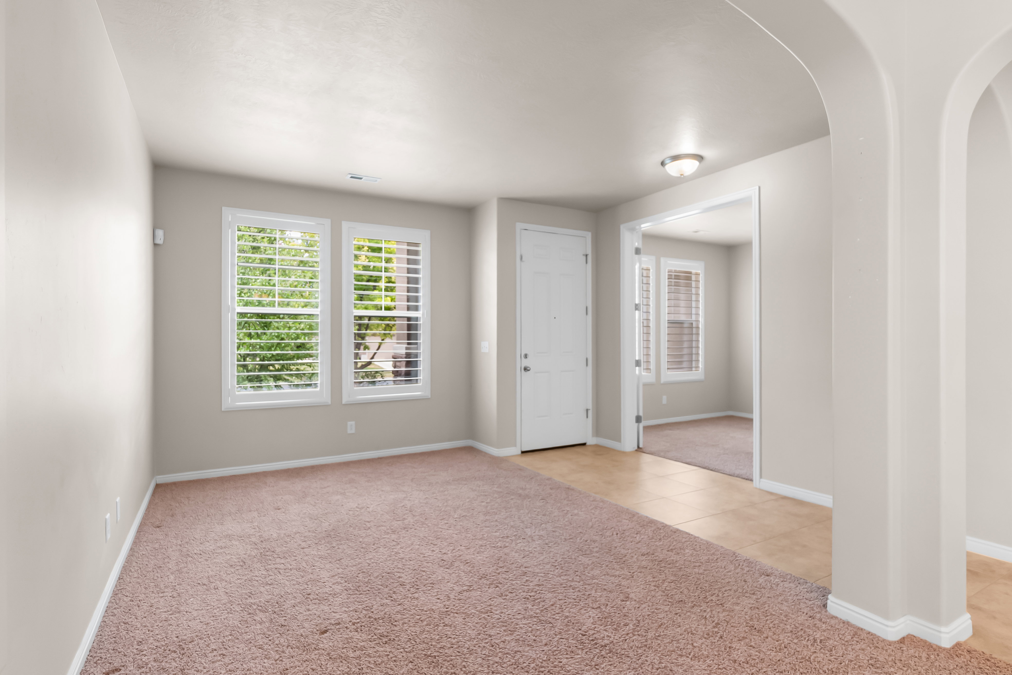 Room featuring neutral wall tones, plush carpeting, two windows with plantation shutters, a white paneled door, and a light fixture