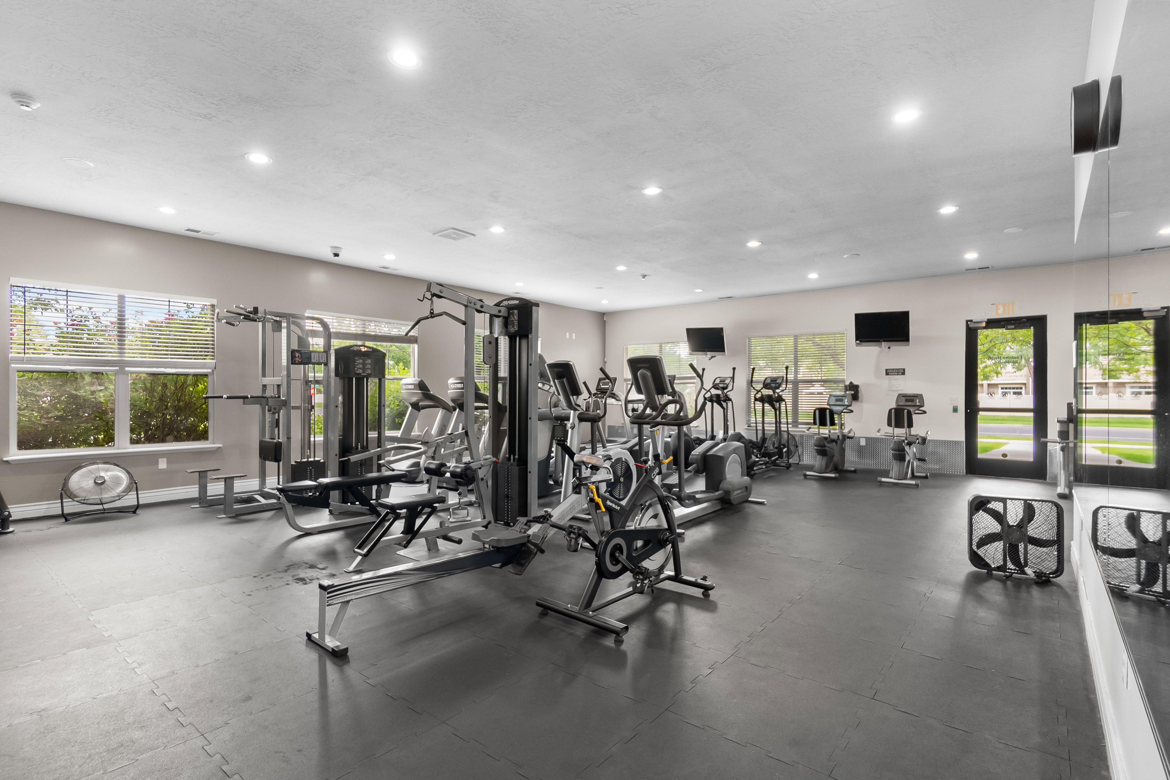 Fitness center featuring extensive exercise equipment, rubberized flooring, abundant natural light from multiple windows, recessed ceiling lighting, and wall-mounted televisions