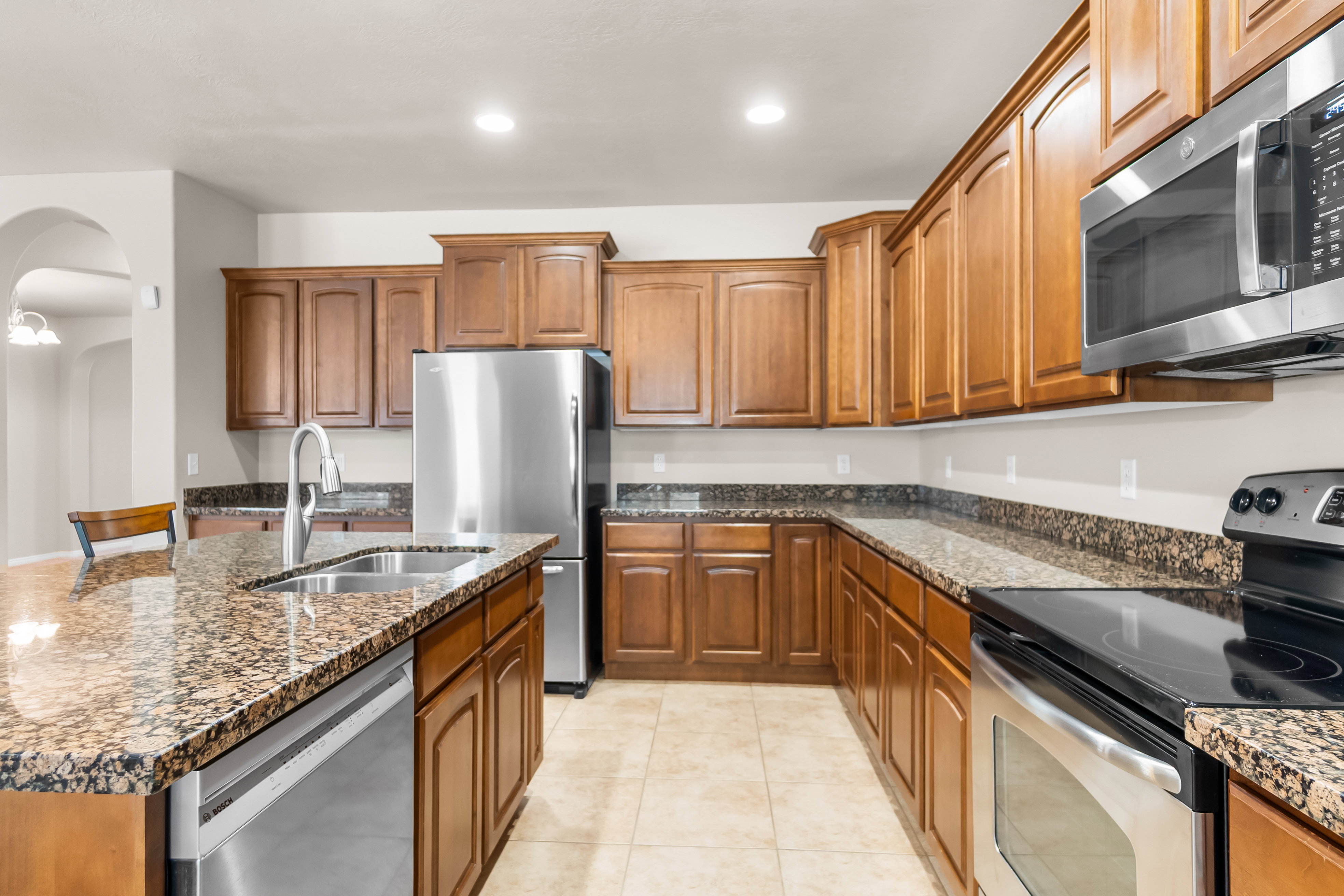 Spacious kitchen featuring warm wood cabinetry, speckled countertops, stainless steel appliances, and a central island with an integrated sink