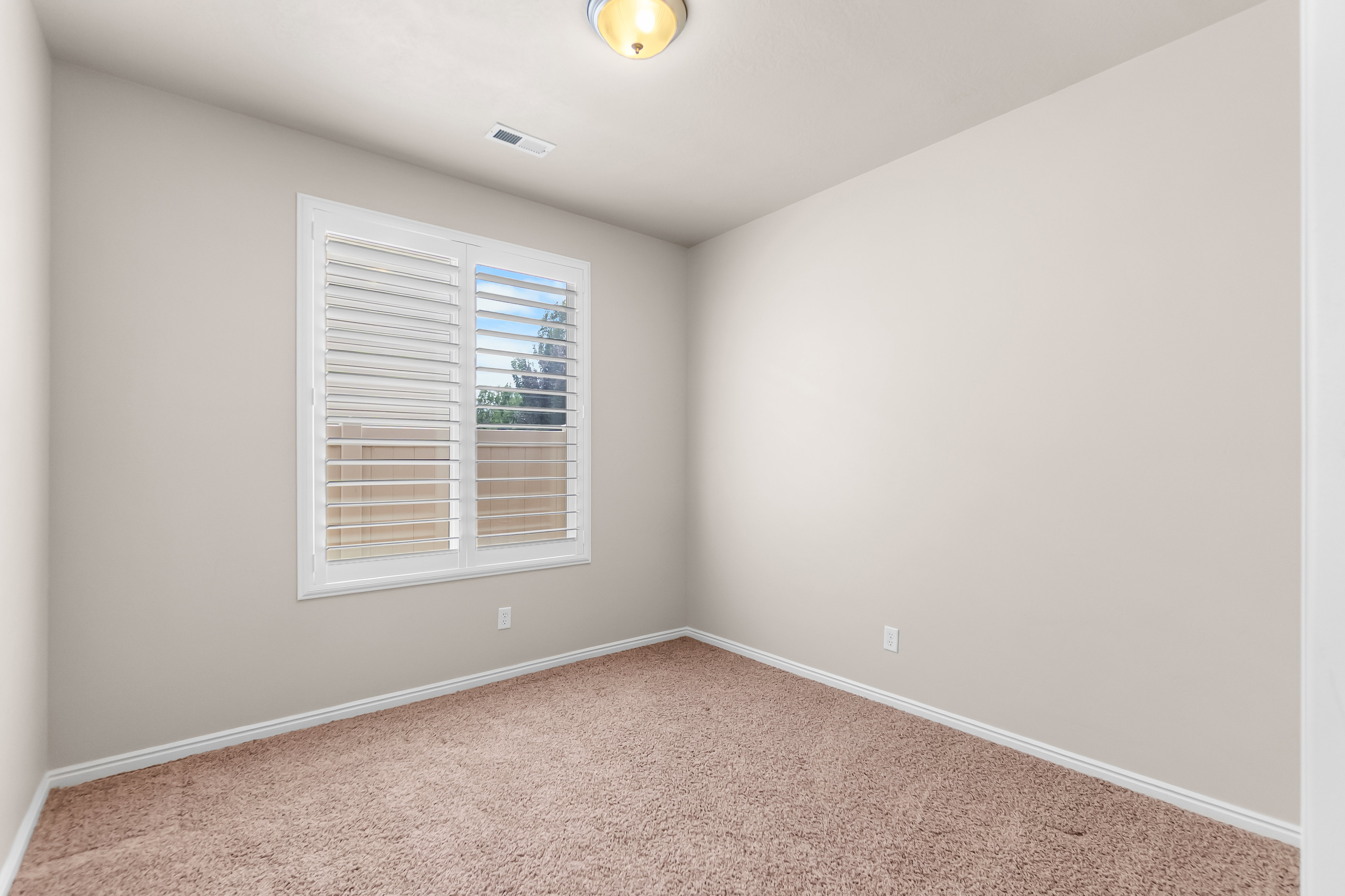 Neutral-toned interior room featuring light brown carpeting and white baseboards
