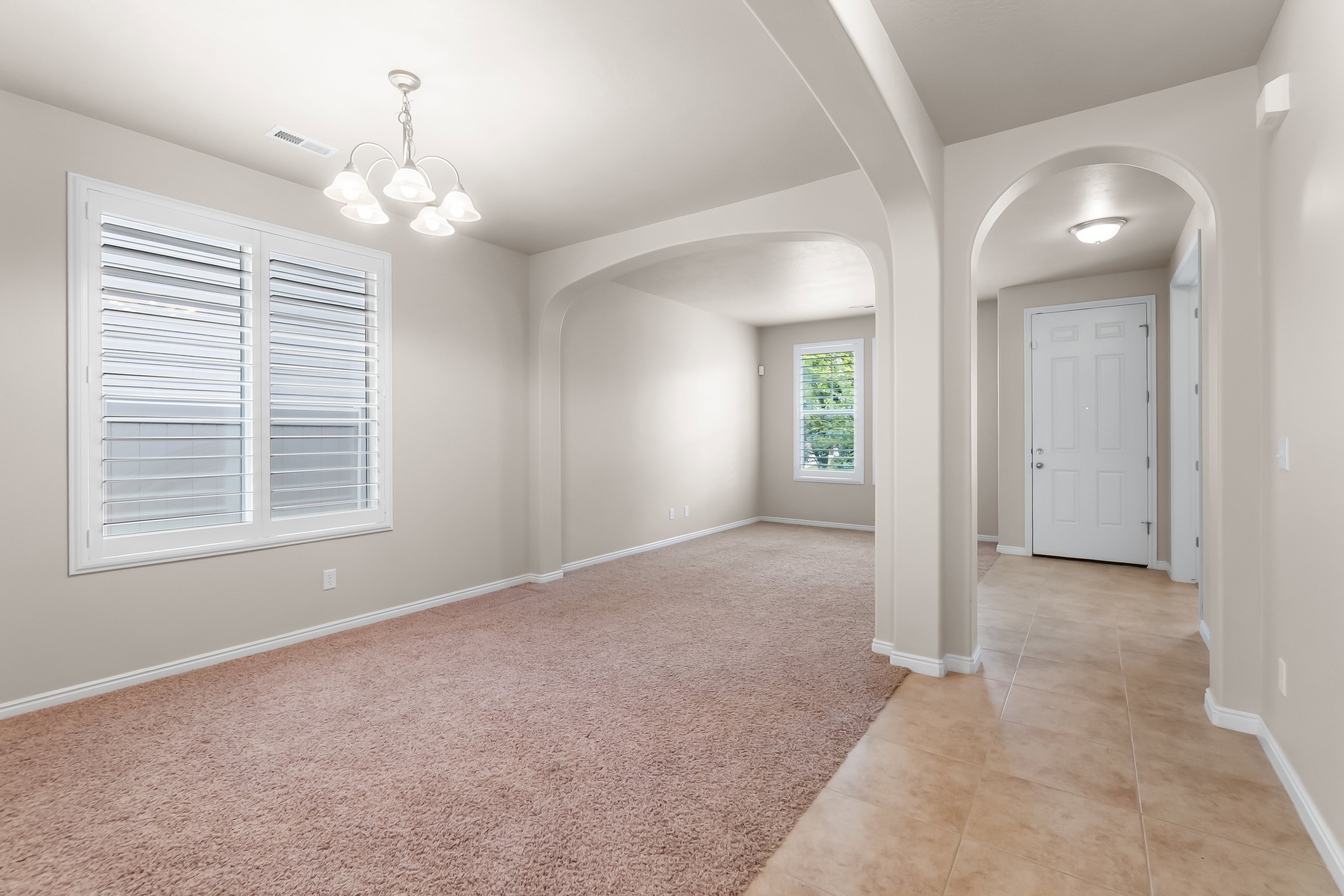Spacious room featuring neutral carpeting, white plantation shutters, and a five-light chandelier