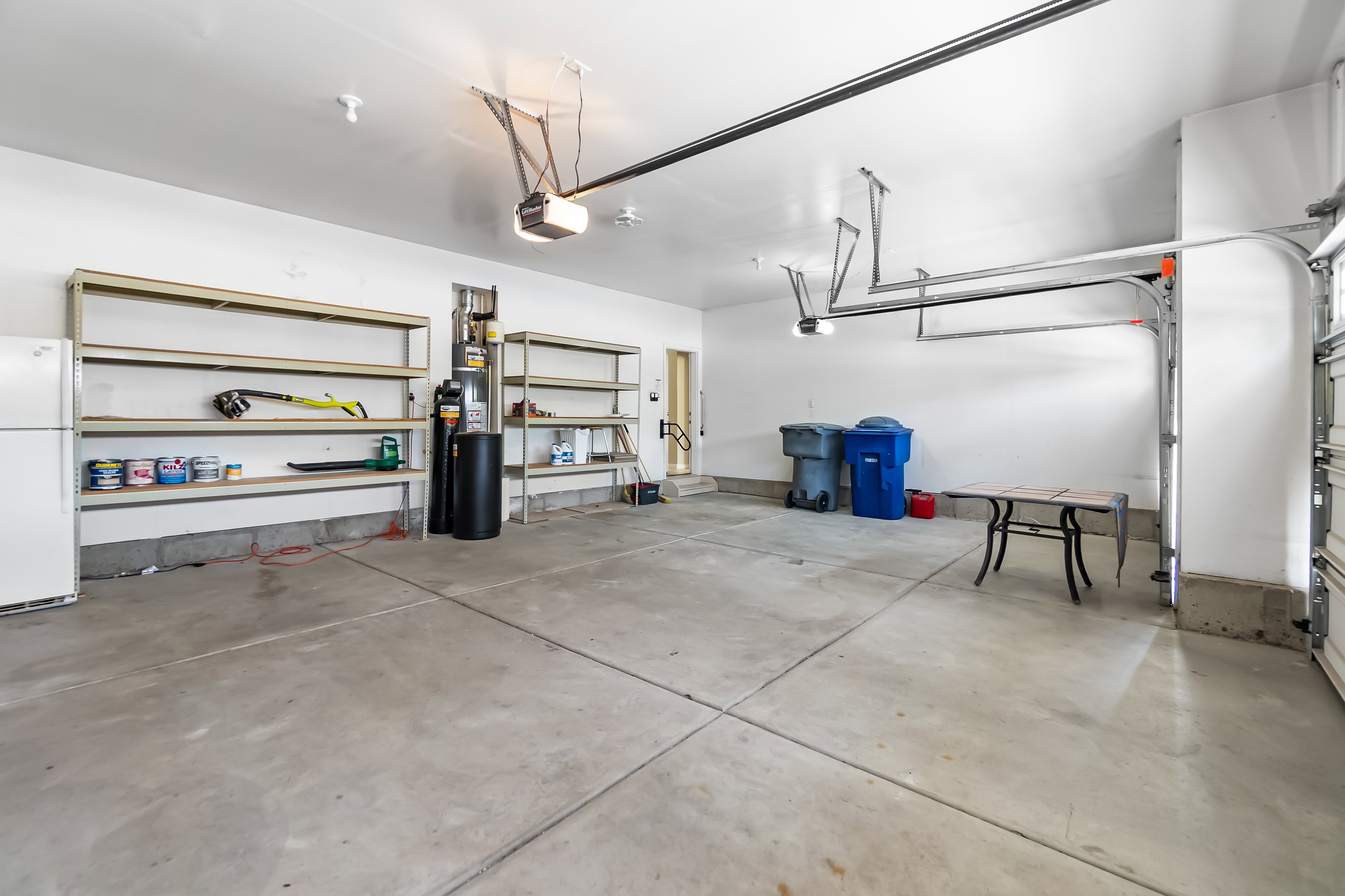 Spacious garage featuring a concrete floor, high ceilings, multiple built-in shelving units, and two overhead garage door openers