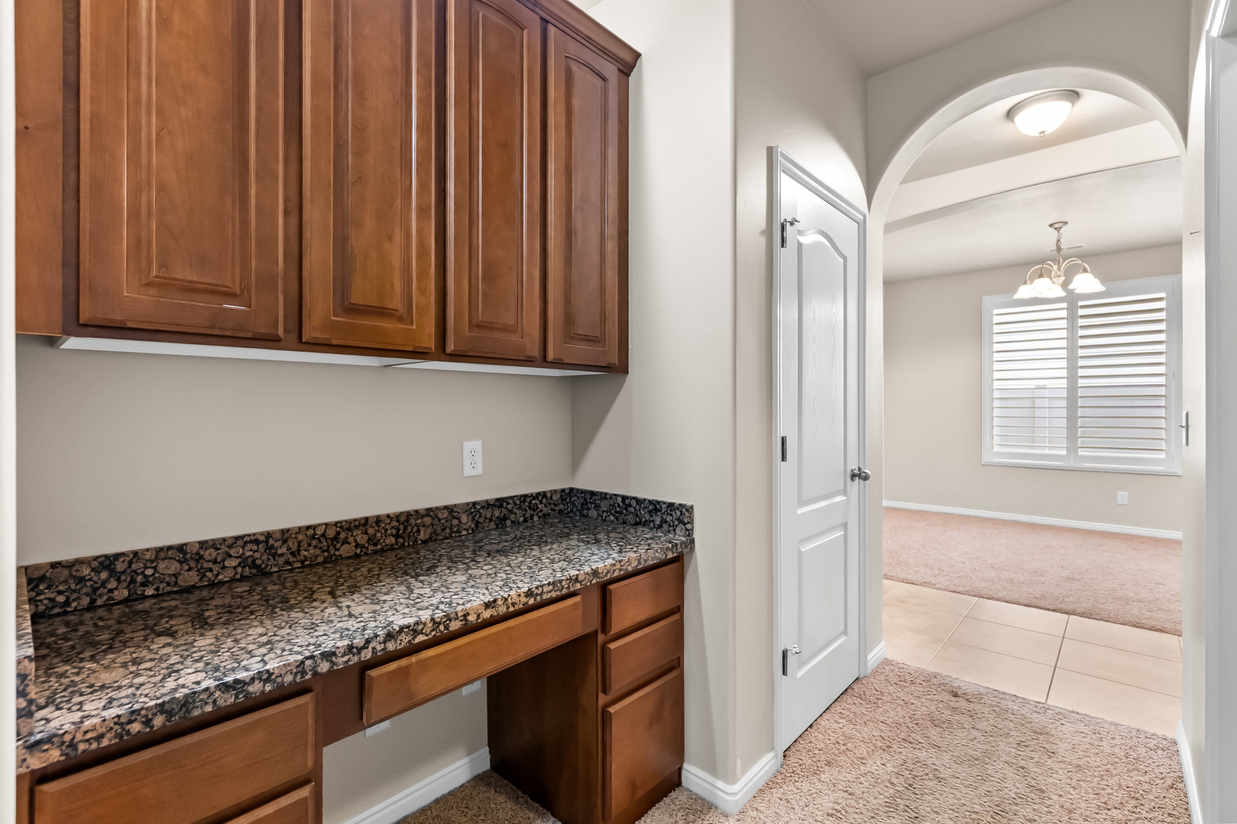 Built-in desk area featuring wood cabinetry, a speckled countertop, and under-cabinet lighting
