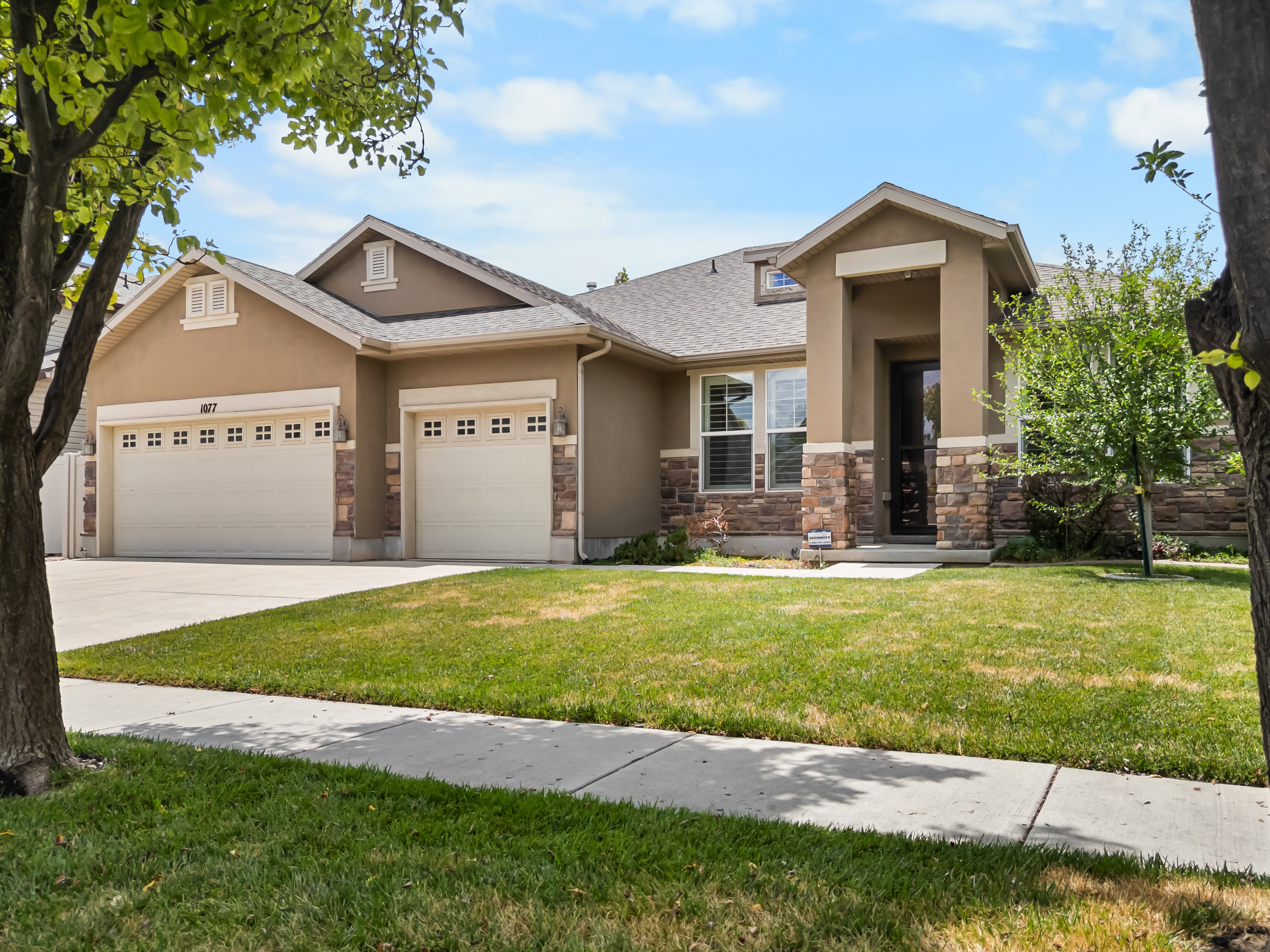 Stucco exterior with stone veneer accents, multi-pane garage doors, covered entry, and a concrete driveway