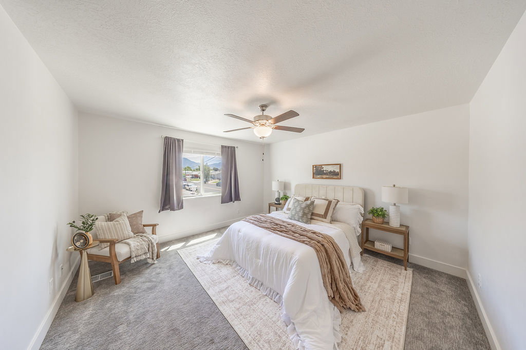 LARGE primary bedroom.  Neutral wall color, ceiling fan with light fixture, window with drapery, and carpeted flooring.