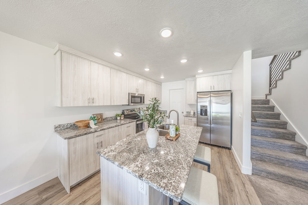 Modern kitchen featuring light wood-finish cabinetry, stainless steel appliances, granite-style countertops, an island with seating, and LVP flooring
