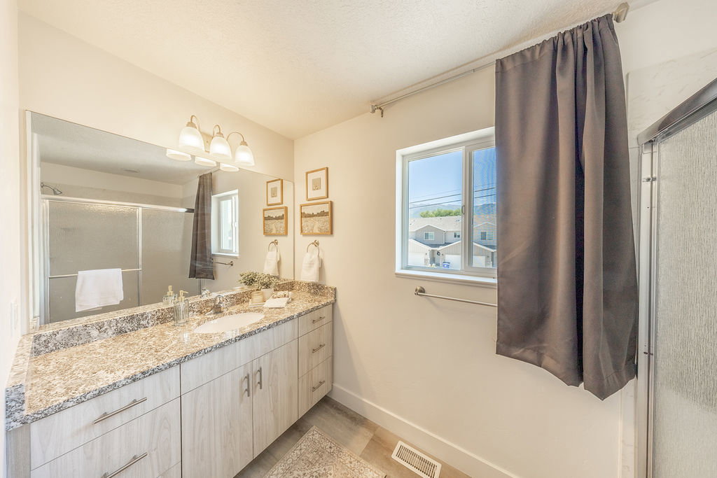 Granite countertop.  Large wall mirror.  Modern light fixture.  Sliding glass doors to shower viewable in mirror.