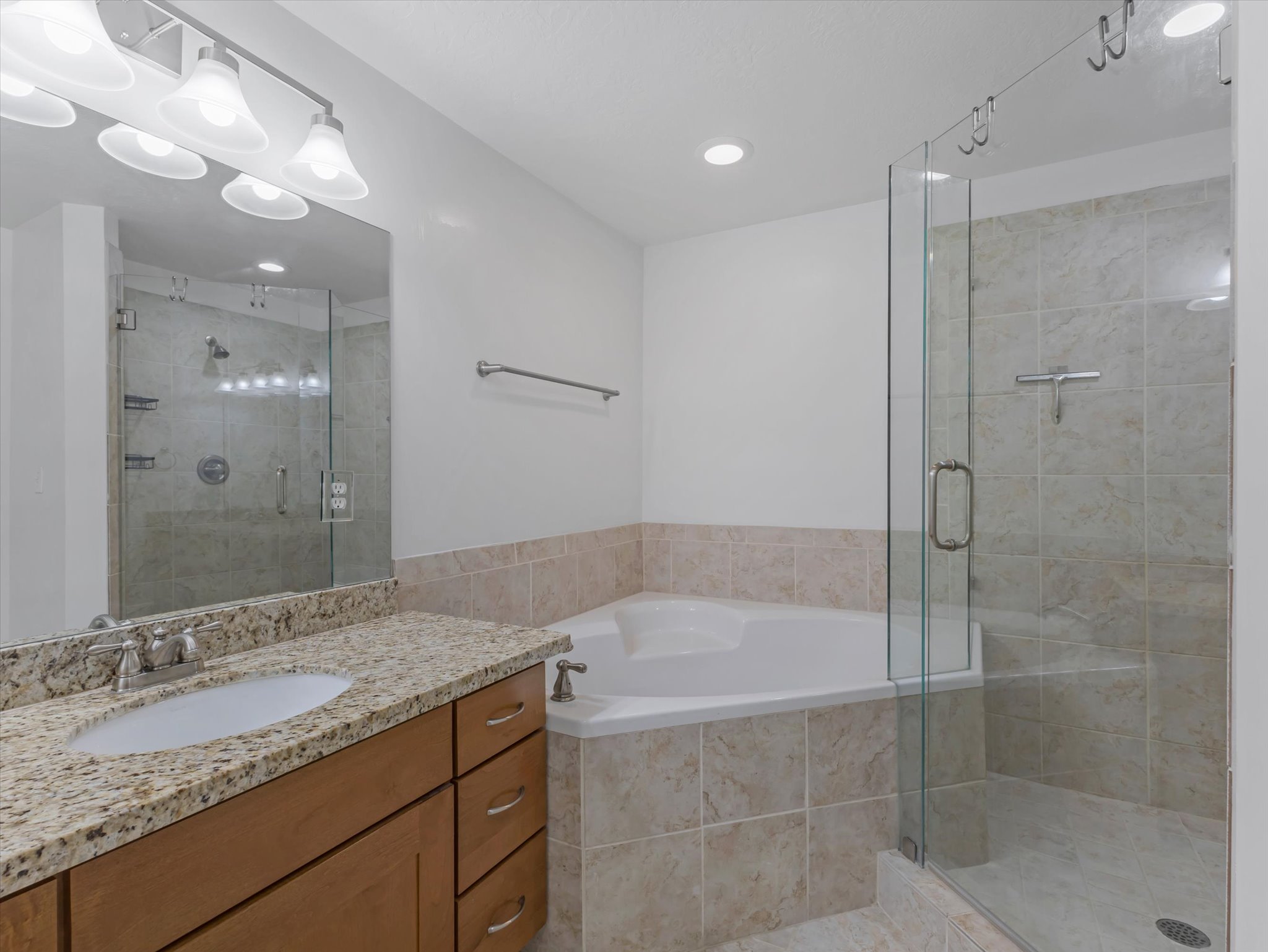 Bathroom featuring a corner soaking tub, glass-enclosed shower with tiled walls, and a vanity with a granite-style countertop