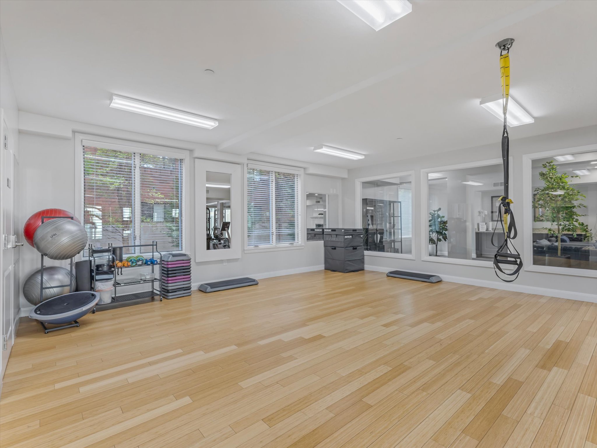Spacious fitness area featuring light wood-finish flooring, recessed lighting, and multiple windows with blinds