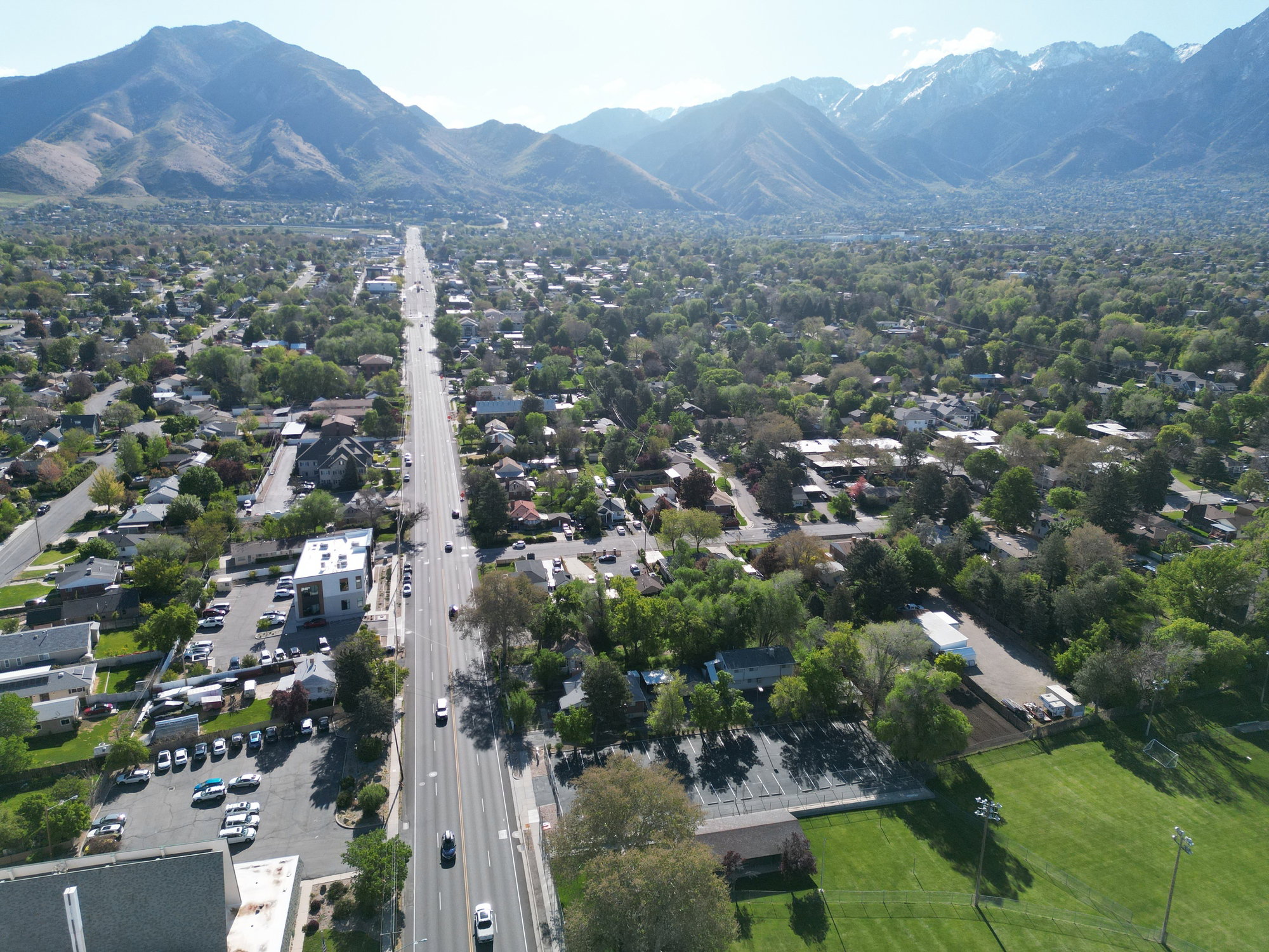 Expansive aerial perspective showcasing a wide thoroughfare, dense tree canopy, and distant mountains
