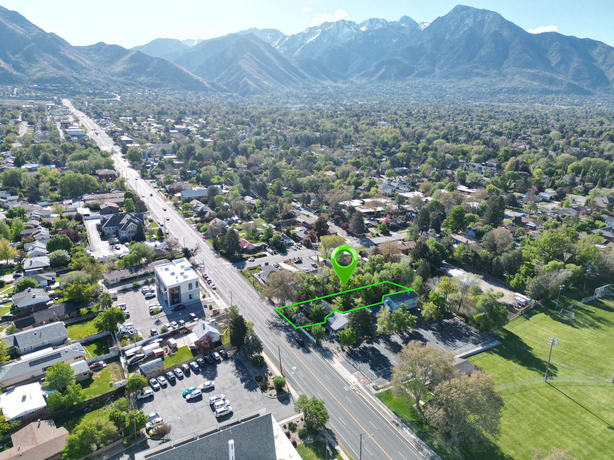 Aerial perspective showcasing a property outlined in green, positioned alongside a broad thoroughfare