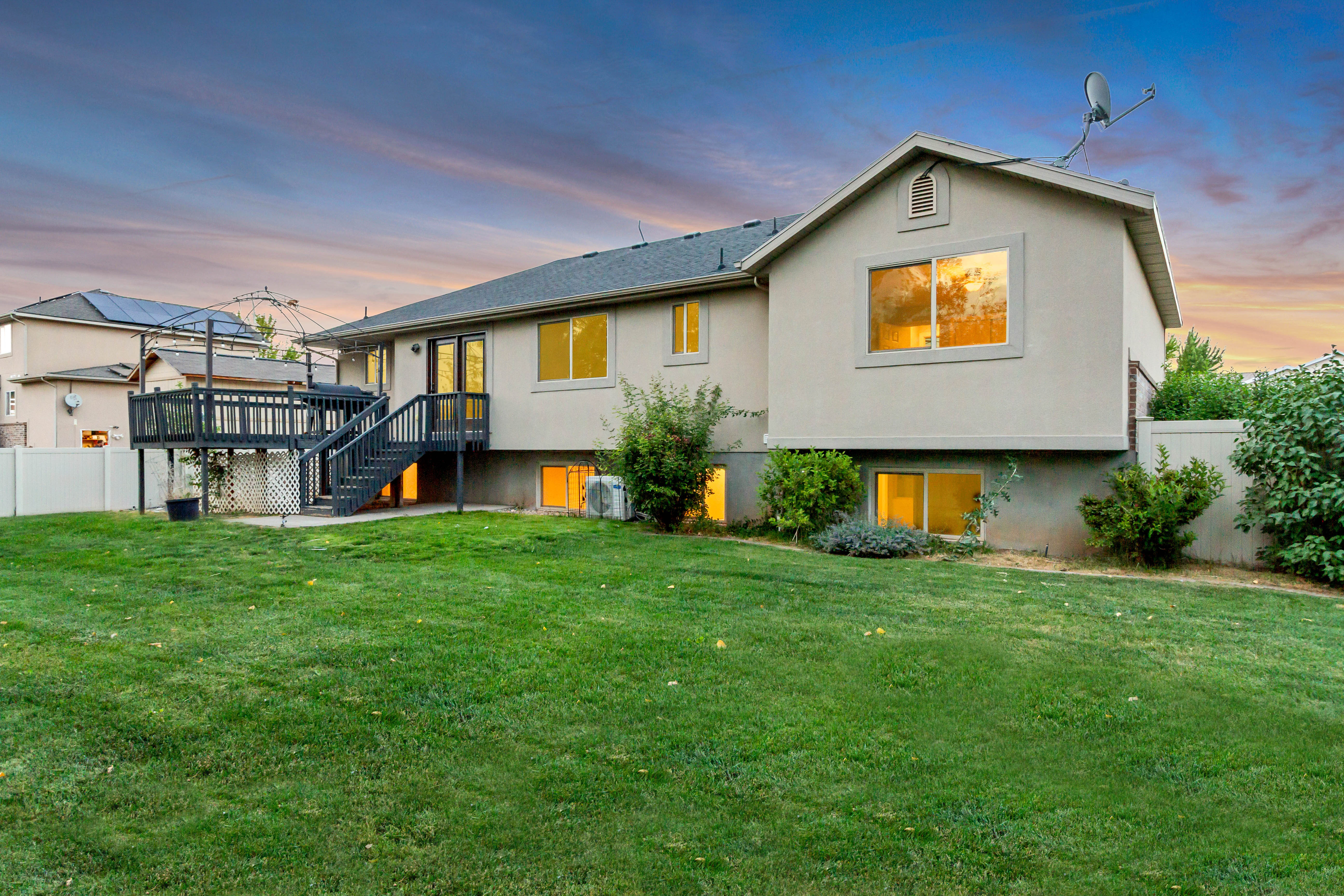 Spacious backyard with a vibrant green lawn, mature landscaping, and a multi-level deck featuring dark wood construction and white railings