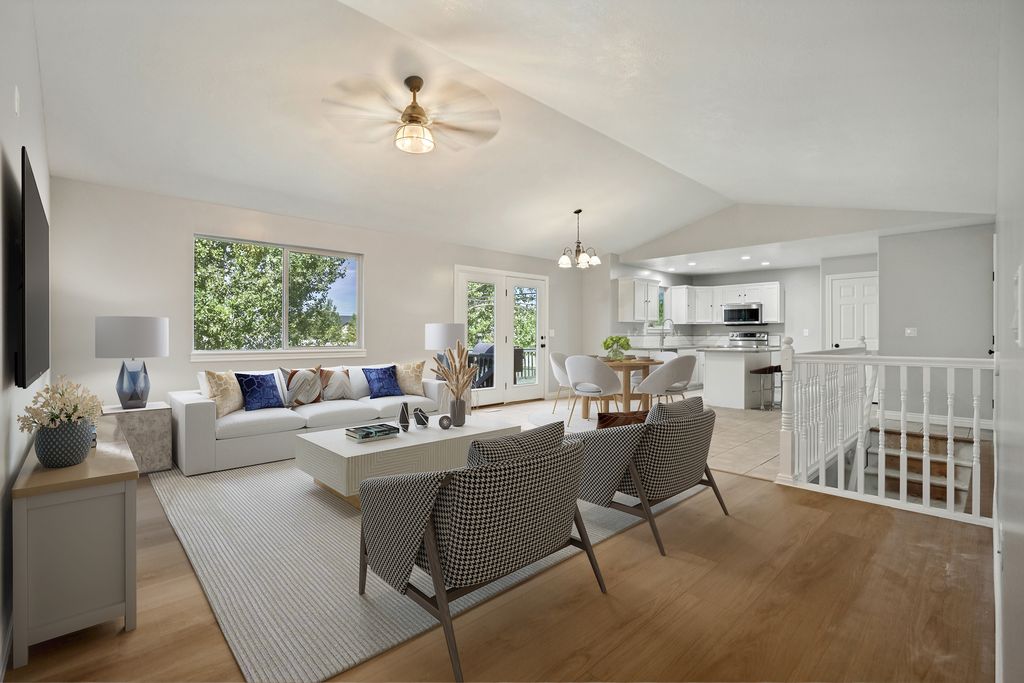 Spacious living area featuring wood-finish flooring, a vaulted ceiling with a ceiling fan, and abundant natural light from a large window