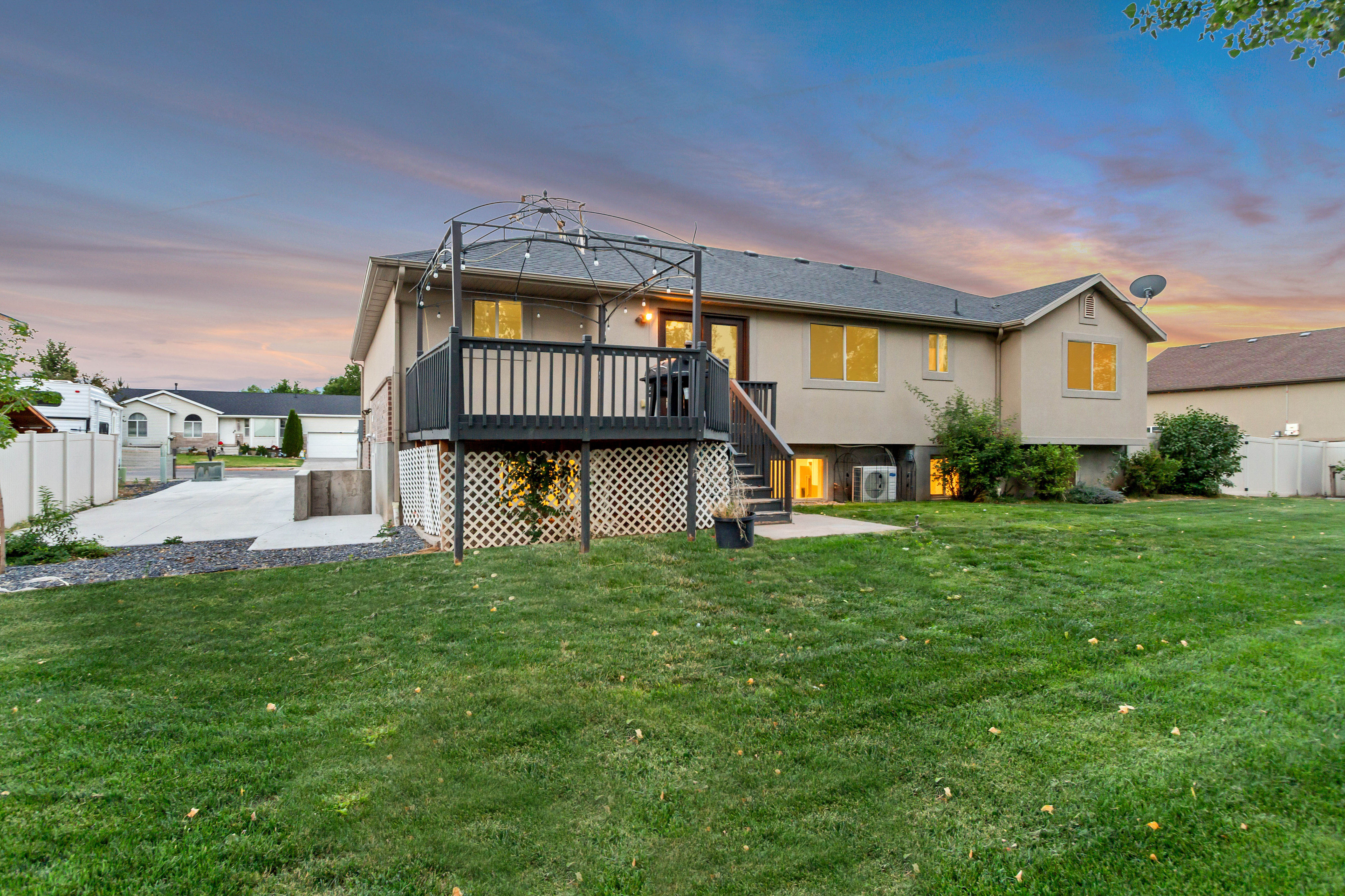 Expansive backyard featuring a manicured lawn, a concrete patio, and a raised wooden deck with railings