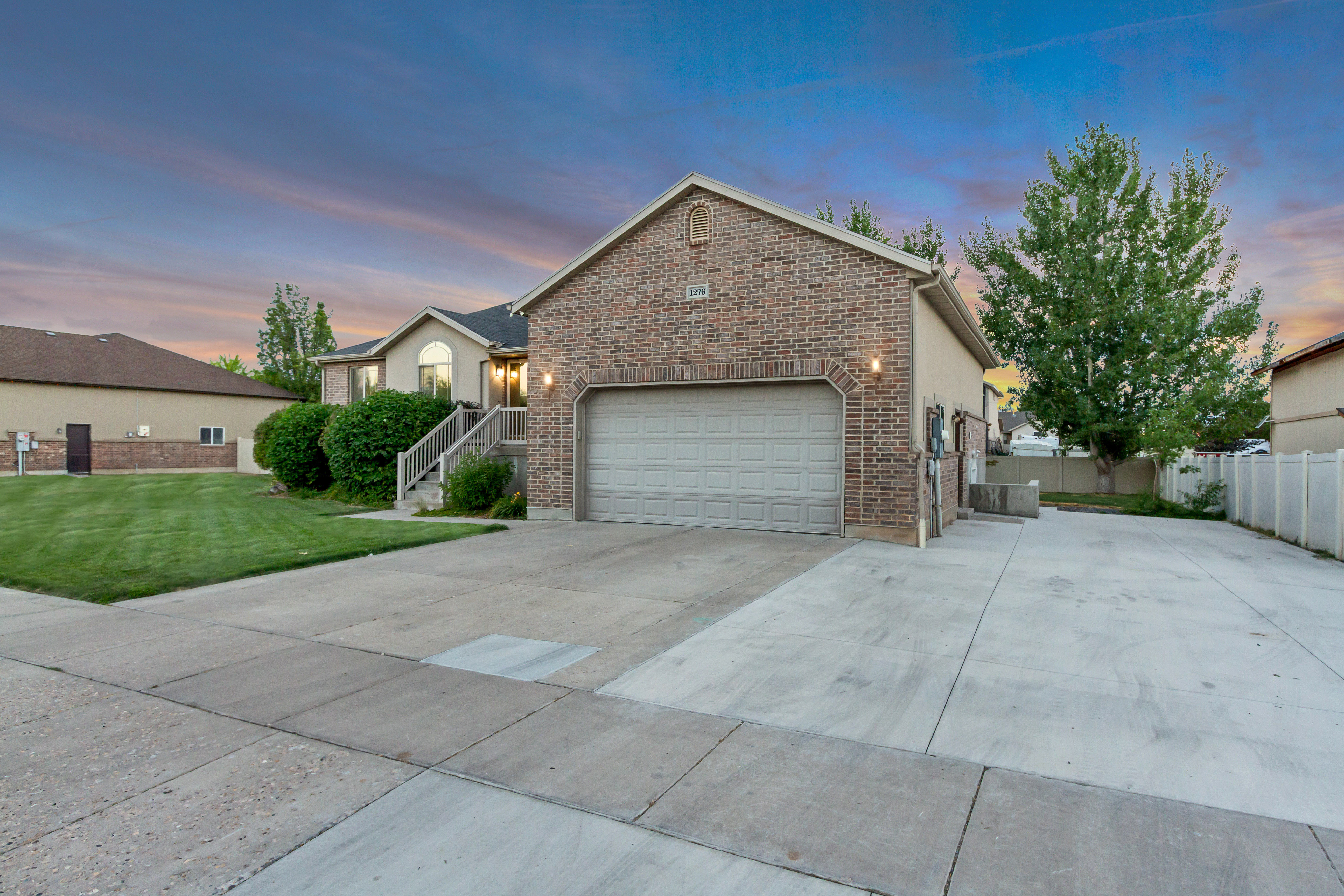 Brick-front residence featuring an attached garage with an automatic door, extensive concrete driveway, and established front yard landscaping