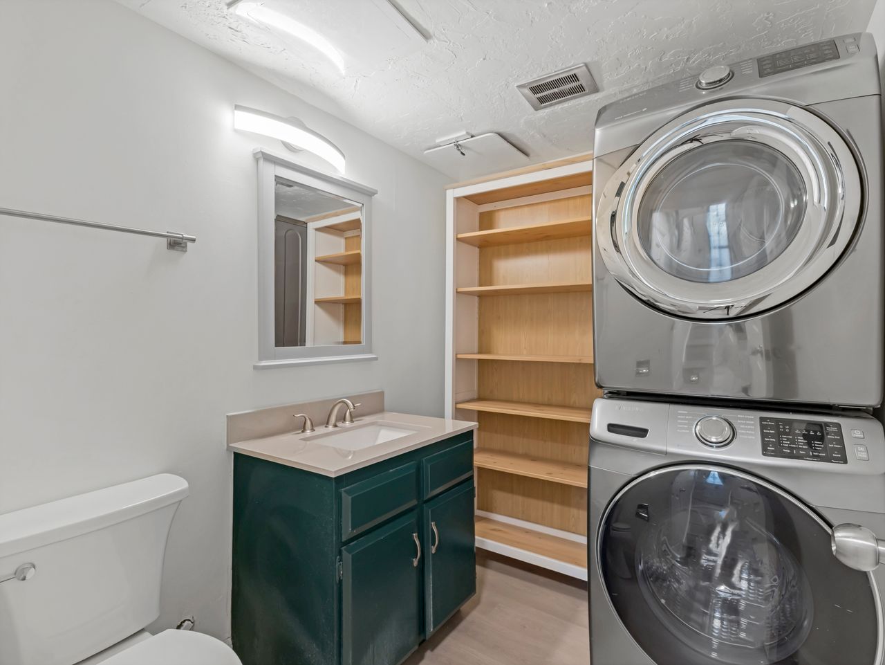 Dedicated utility area featuring a stacked washer and dryer, built-in shelving, a vanity with a dark green cabinet, a rectangular sink, and a framed mirror