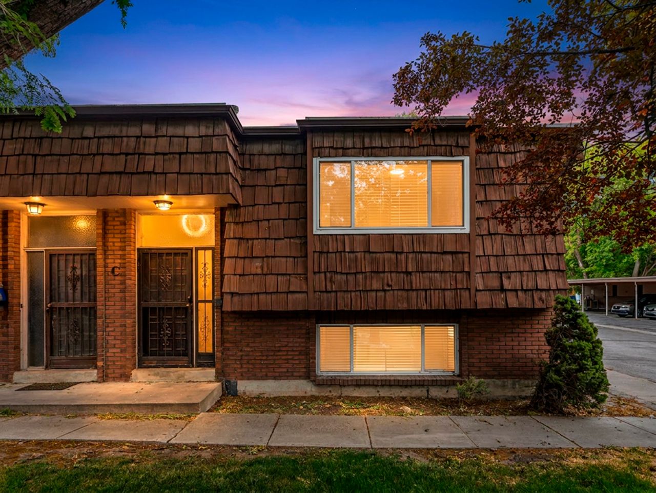 Facade featuring brick and wood shingle-style siding, multiple windows with horizontal blinds, and a concrete walkway