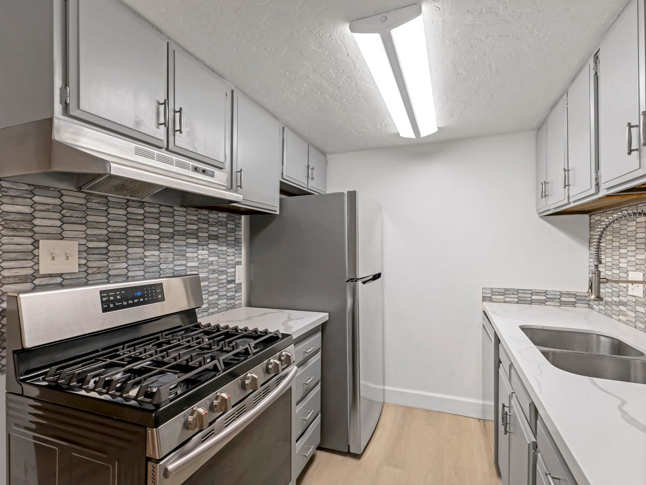 Kitchen featuring light gray cabinetry, stainless steel appliances, patterned tile backsplash, light wood-finish flooring, and white countertops