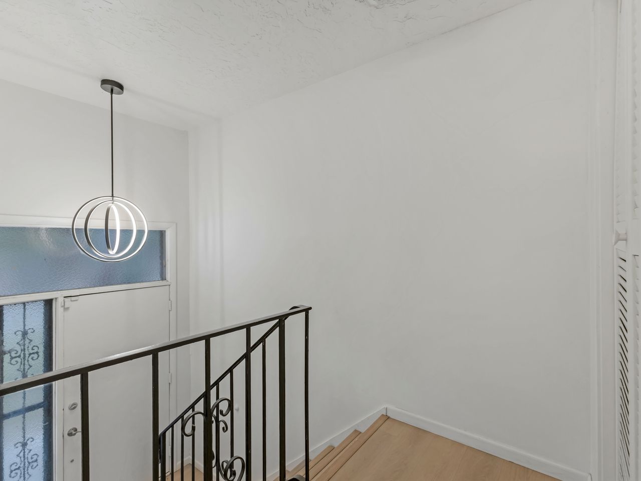 Entryway featuring a modern spherical pendant light, frosted glass door with decorative panels, wrought iron stair railing, and light wood-finish flooring